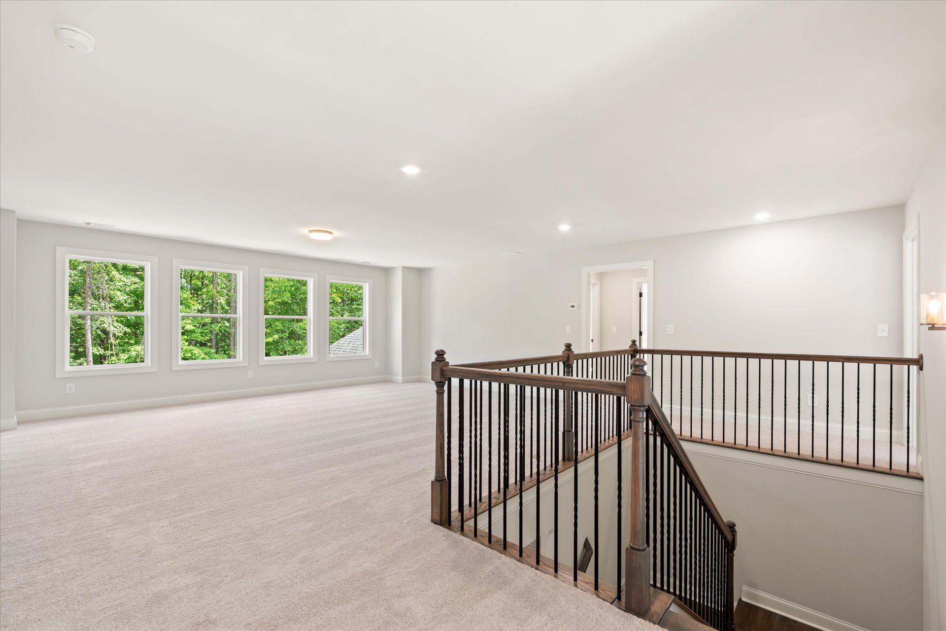 Bright carpeted upstairs landing with white walls, windows, and a staircase railing overlooking below