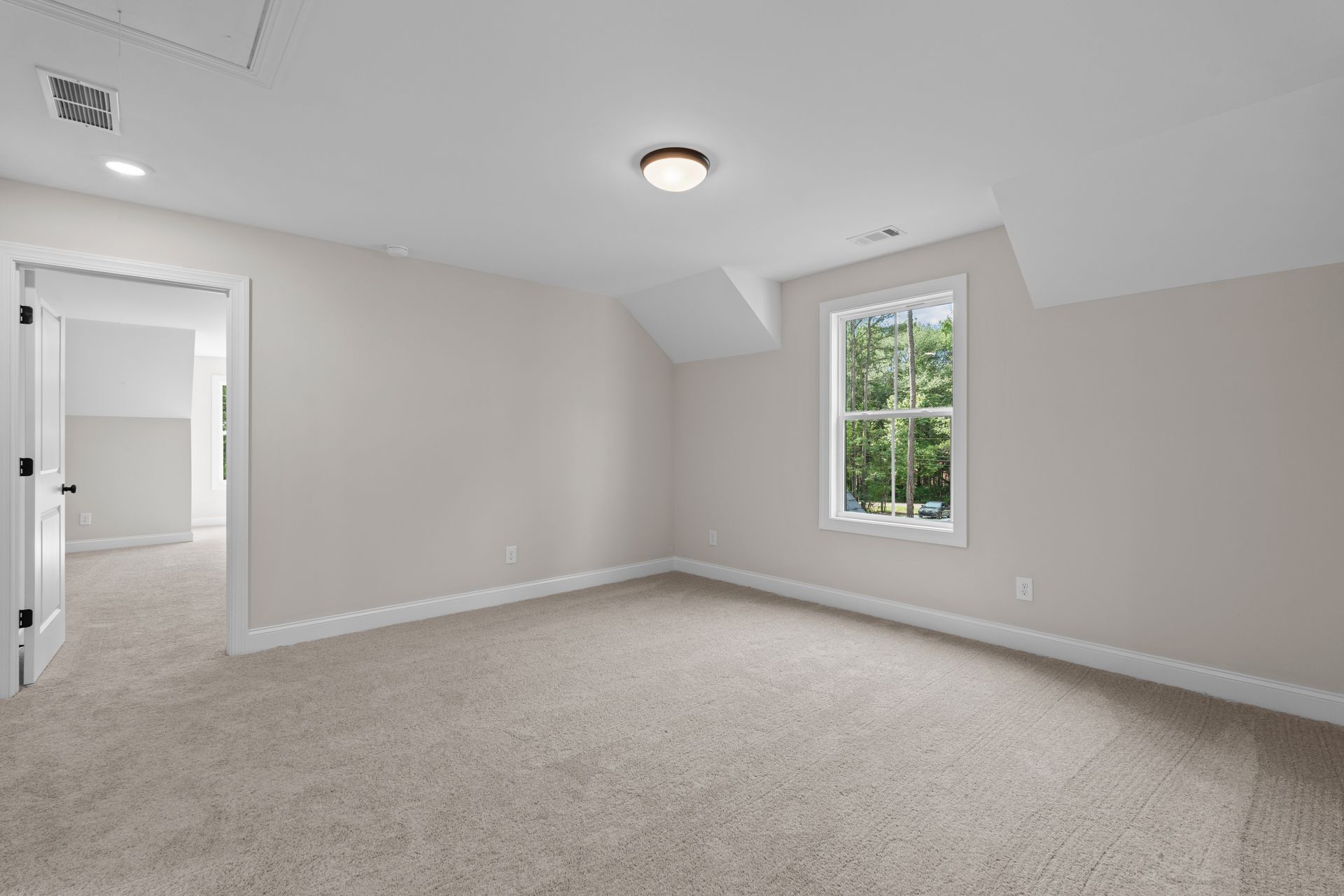 Empty beige bedroom with carpet, white walls, and a window letting in natural light