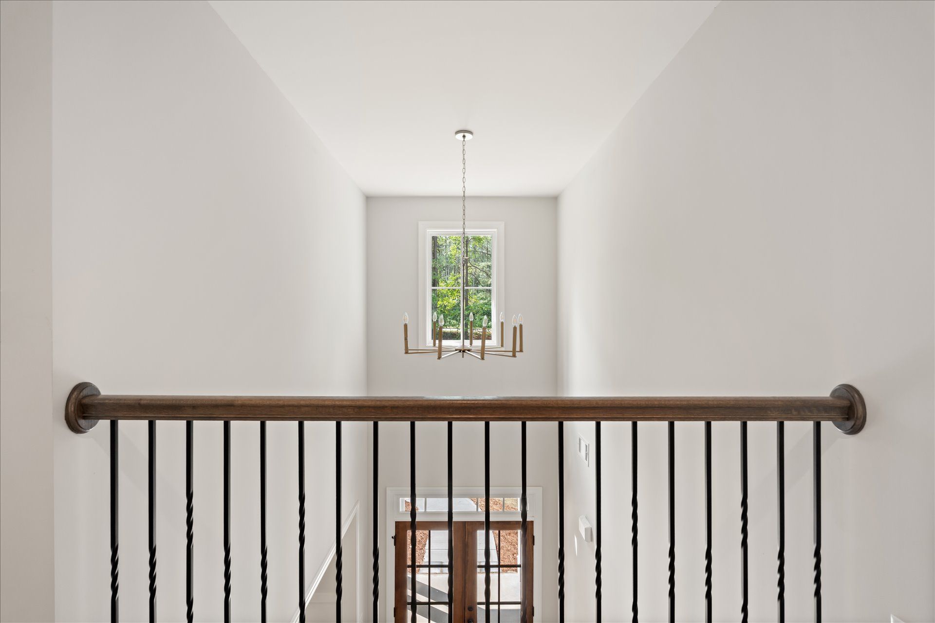 Interior hallway with black railing, white walls, and a window at the far end