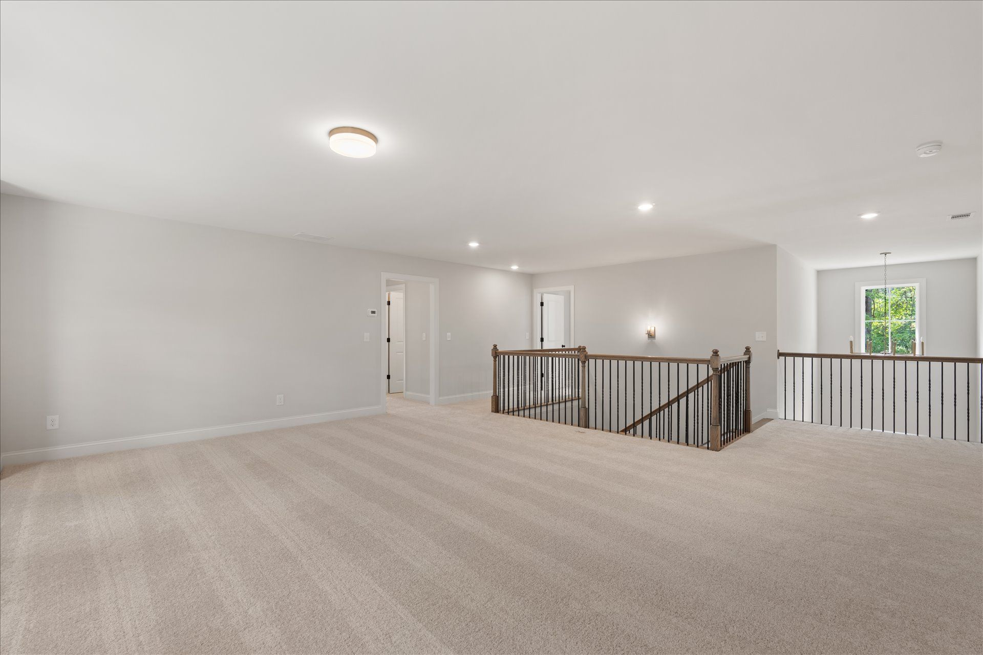 Spacious empty upstairs hallway with beige carpet, white walls, and black railing overlooking the lower floor