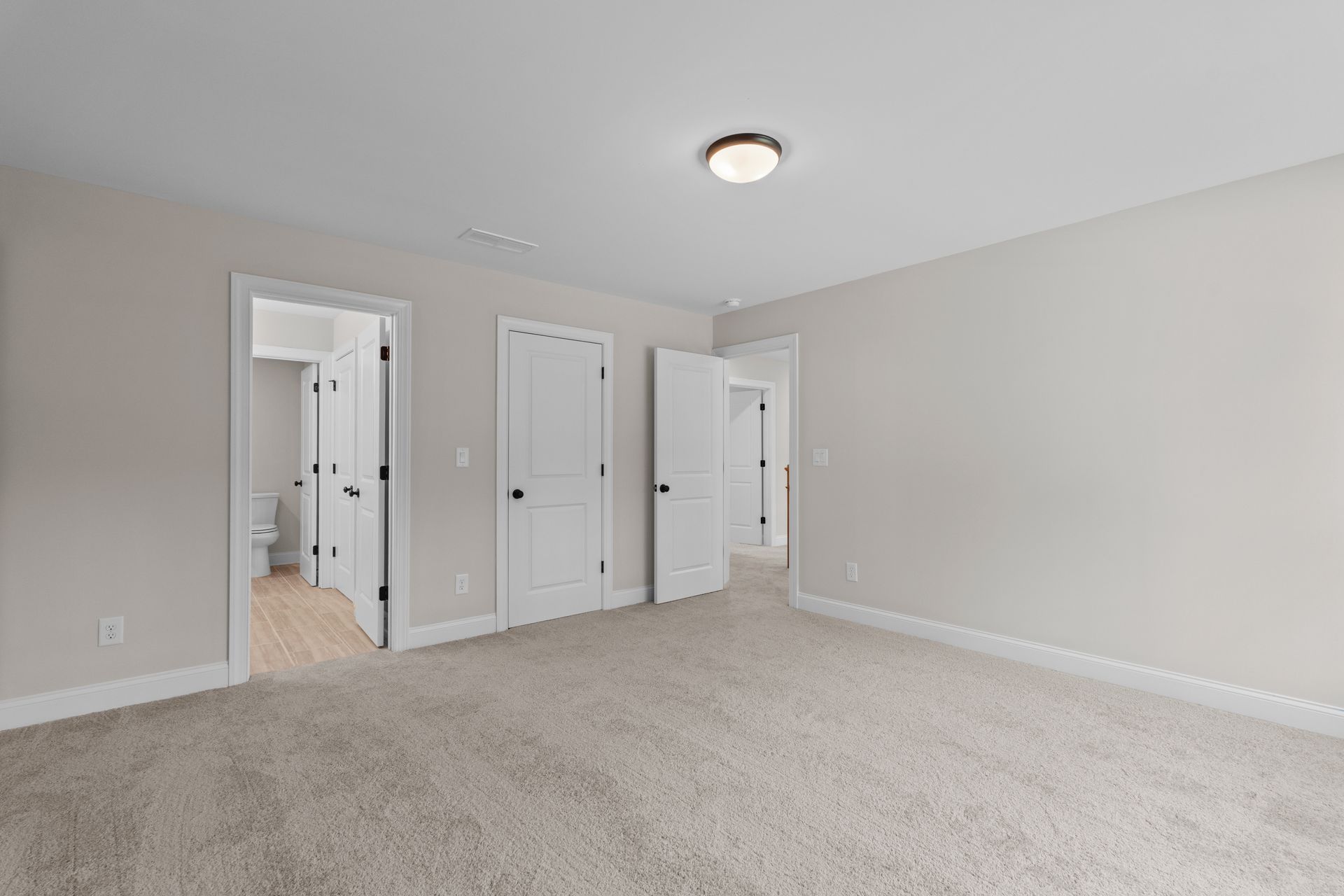 Empty beige bedroom with carpet, white trim, two closets, and an open door to a hallway