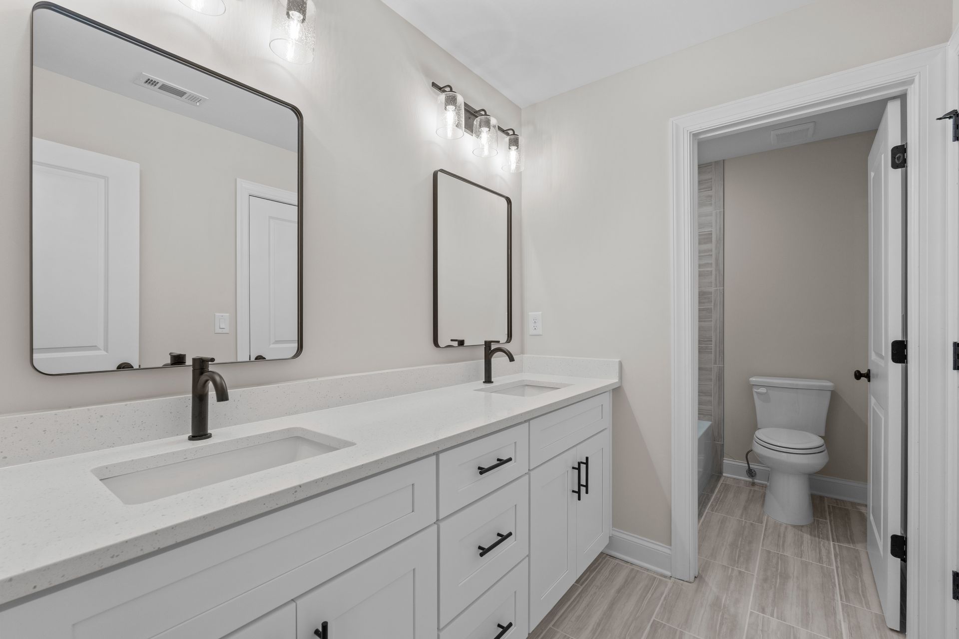 Modern white bathroom with double vanity, large mirrors, and an open doorway to a toilet room
