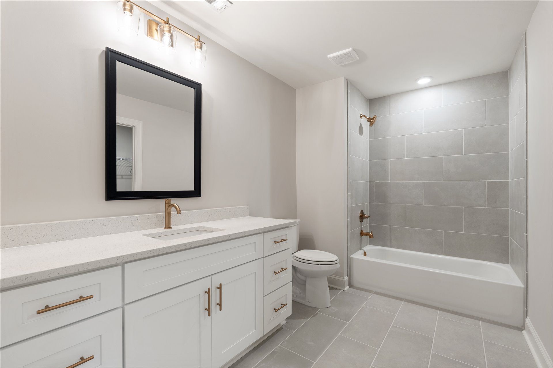 Bright modern bathroom with white vanity, black-framed mirror, and tiled shower/tub combo