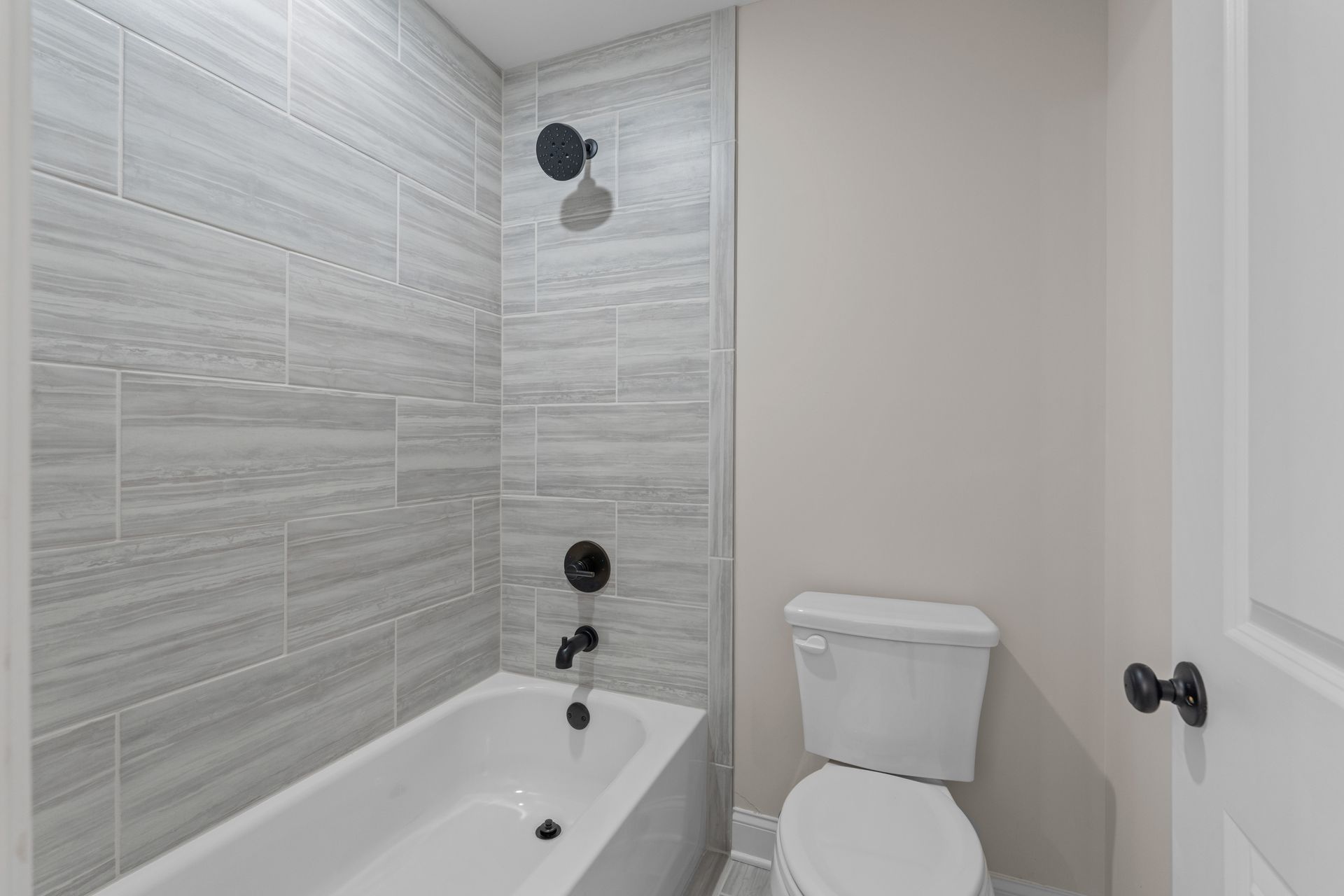 Small white bathroom with bathtub, tiled shower wall, toilet, and door.