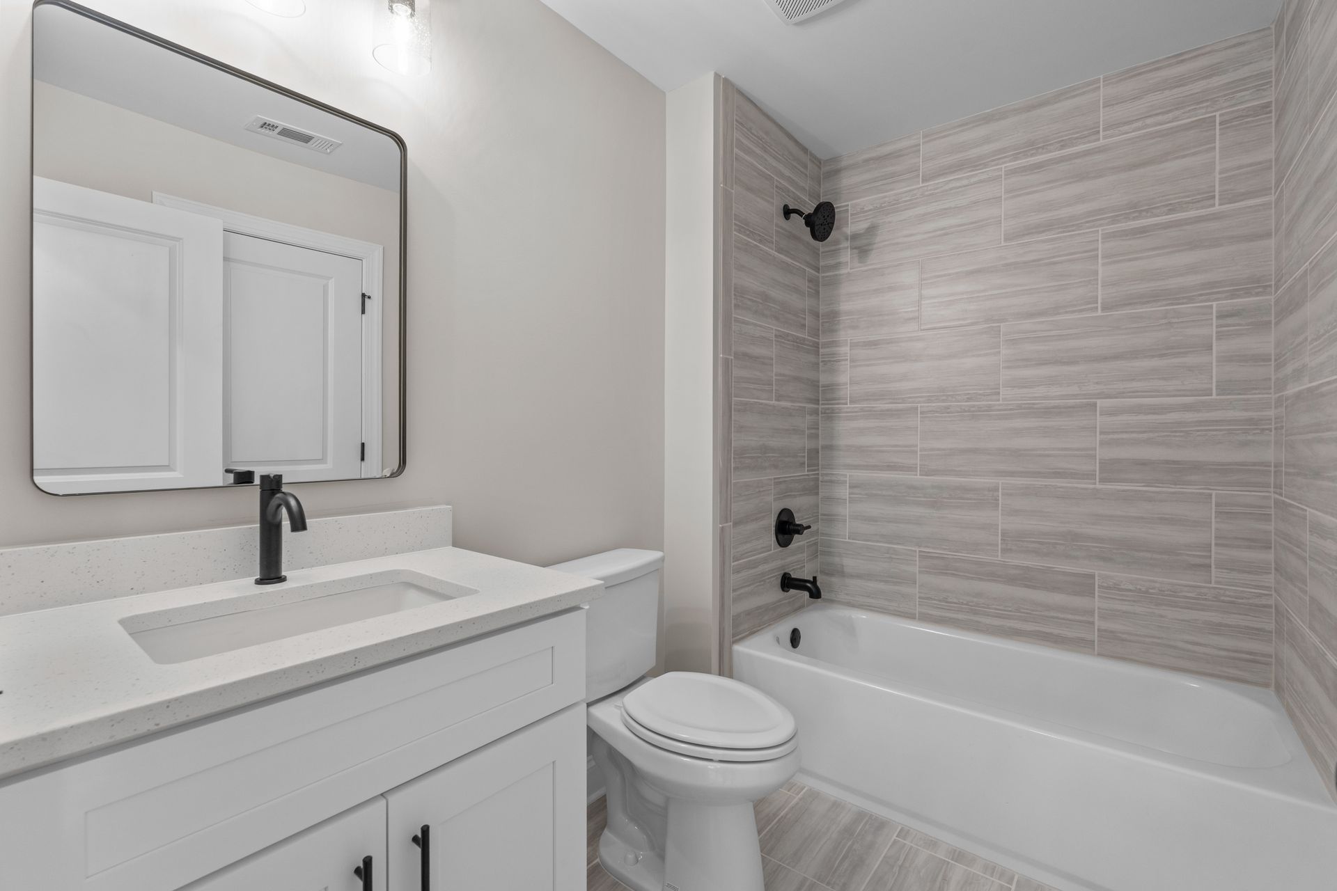 Modern bathroom with white vanity, mirror, toilet, and tiled bathtub/shower alcove