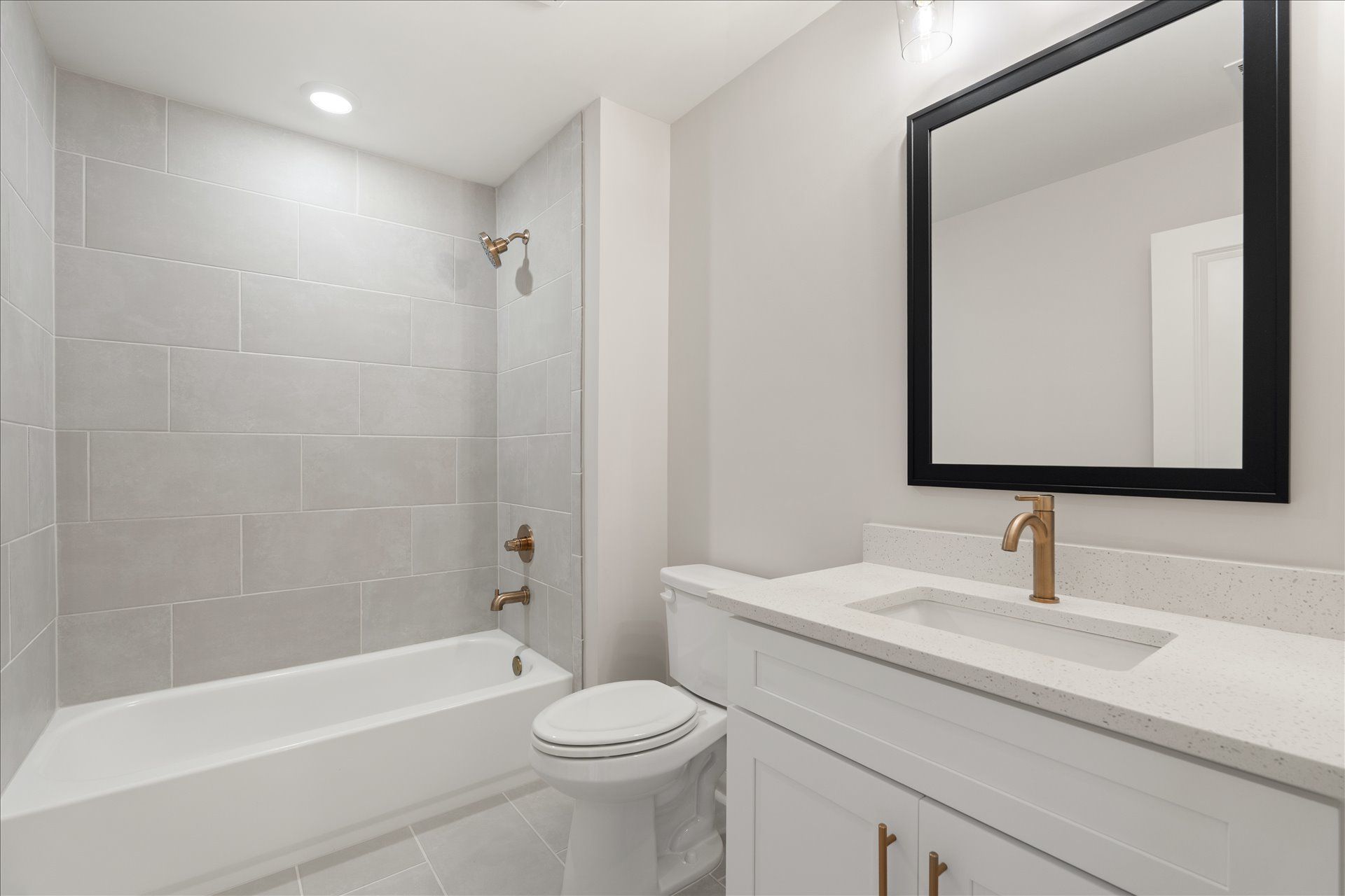Bright modern bathroom with white tub, toilet, vanity, and black-framed mirror