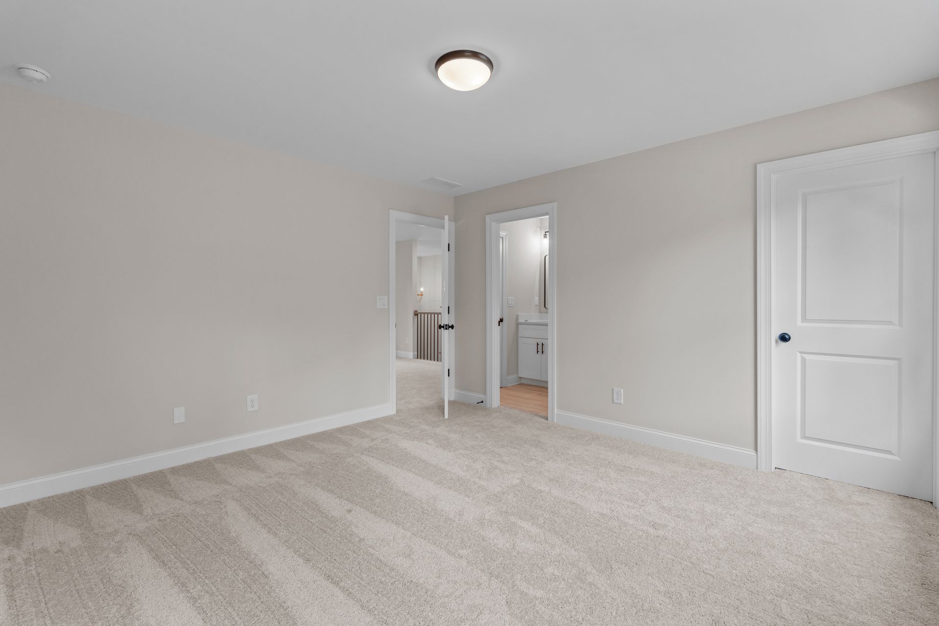 Empty beige bedroom with carpet, ceiling light, closet, and an open doorway to a bathroom.