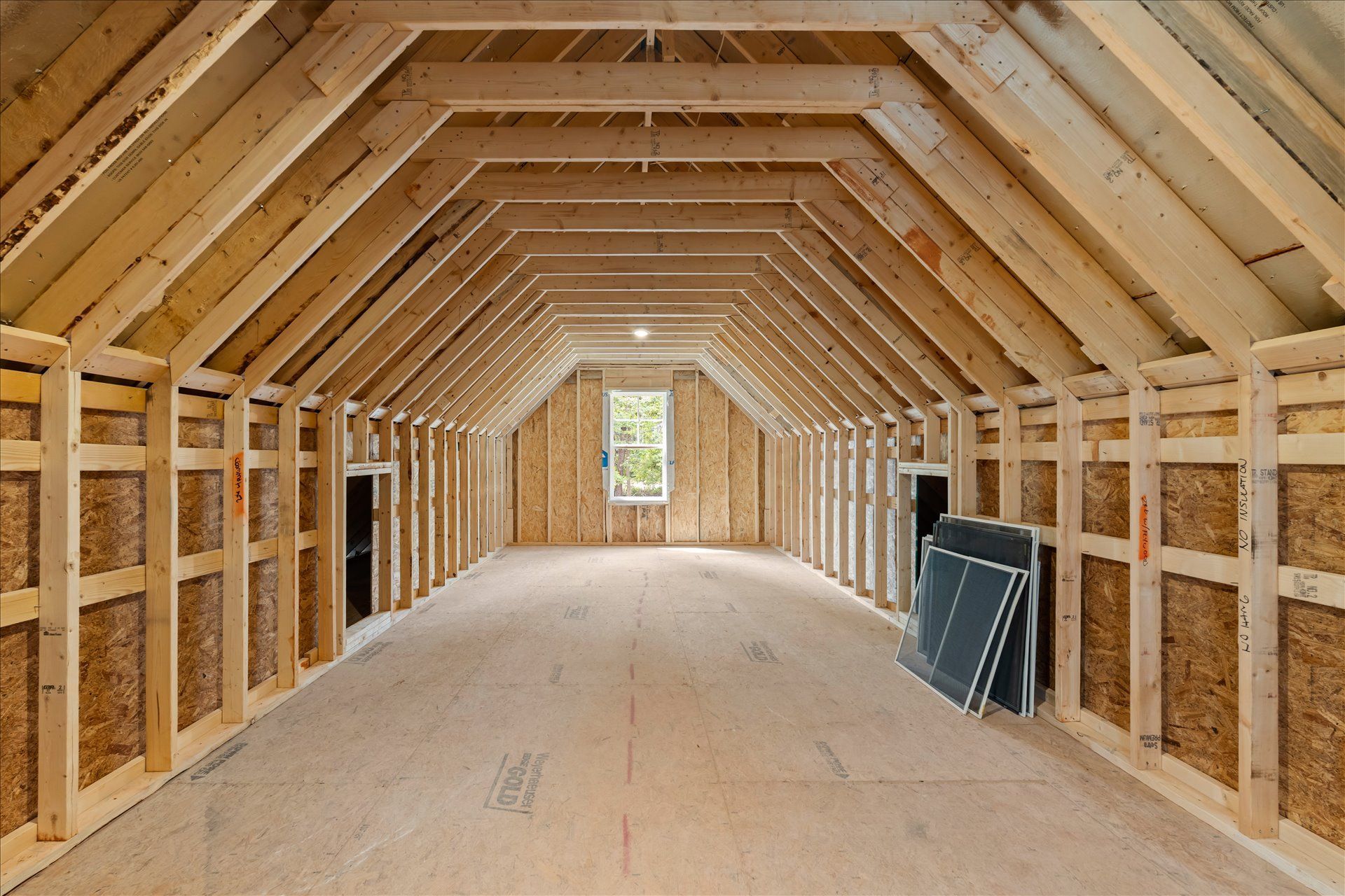 Unfinished wooden interior with exposed roof trusses and insulation, viewed down a long hallway.