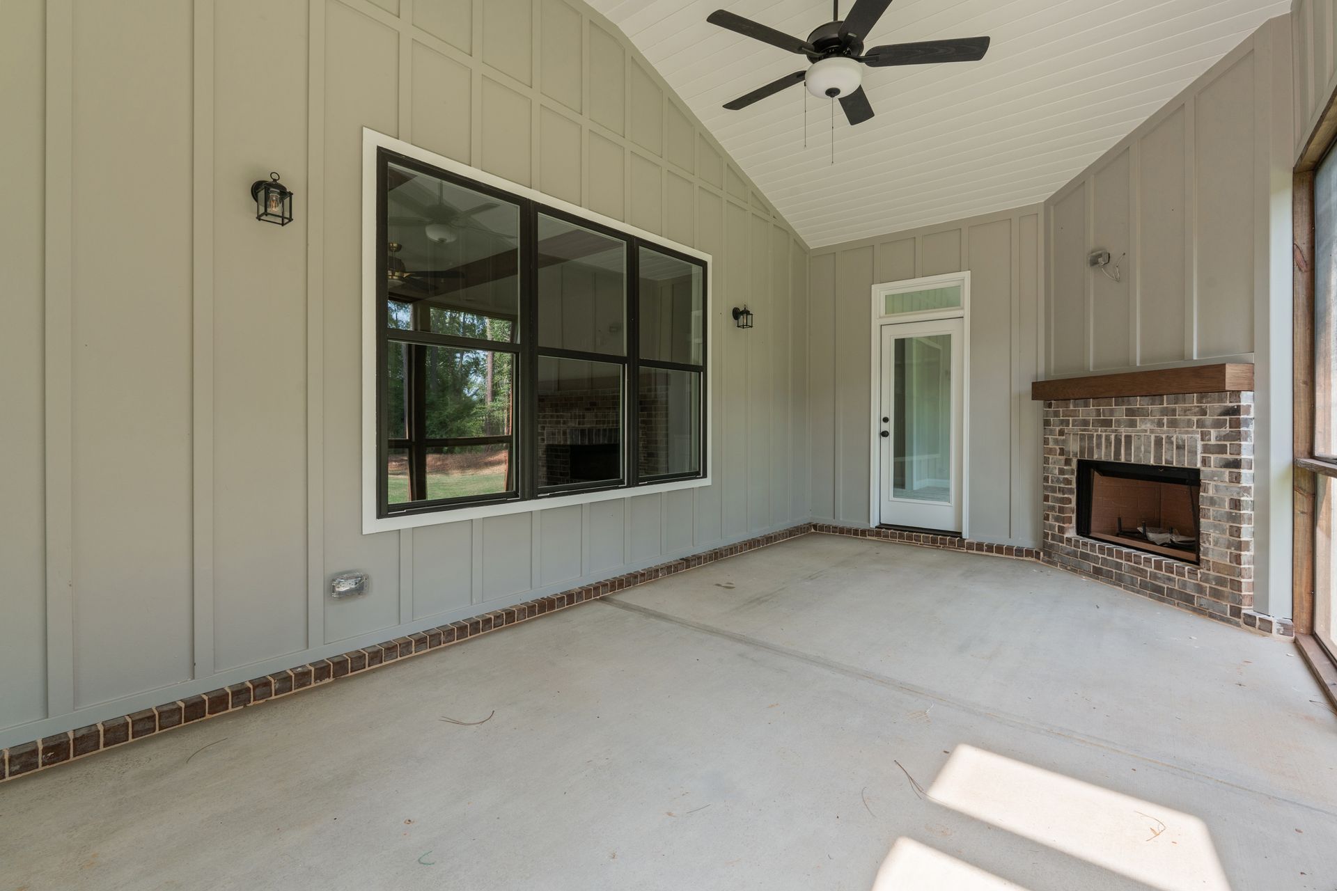 Covered patio with beige walls, ceiling fan, large window, and brick fireplace.
