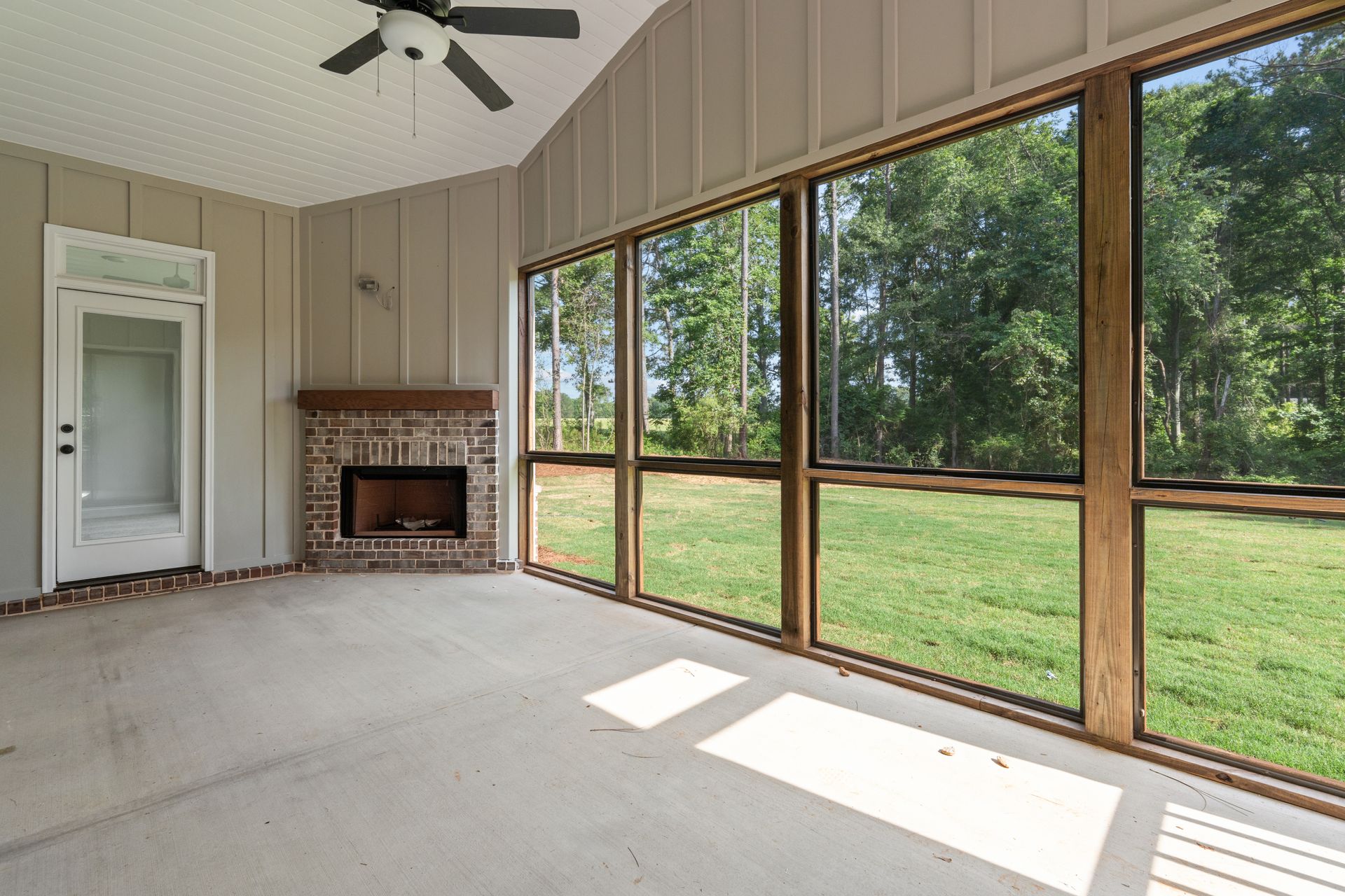 Empty sunroom with fireplace, ceiling fan, and large windows overlooking a grassy yard.