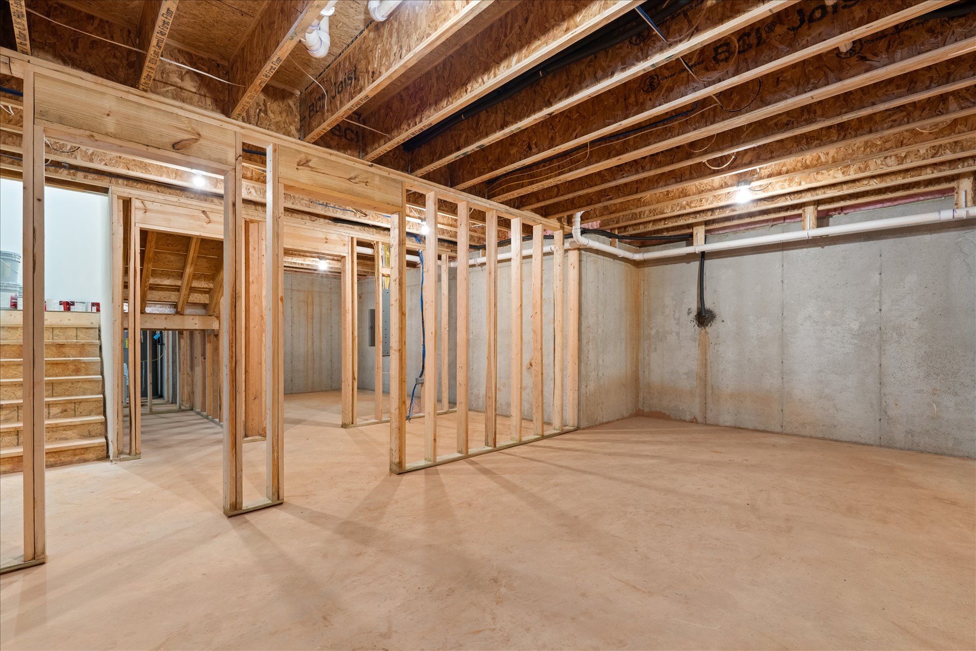 Unfinished basement interior with exposed wood framing, beams, and concrete walls and floor.