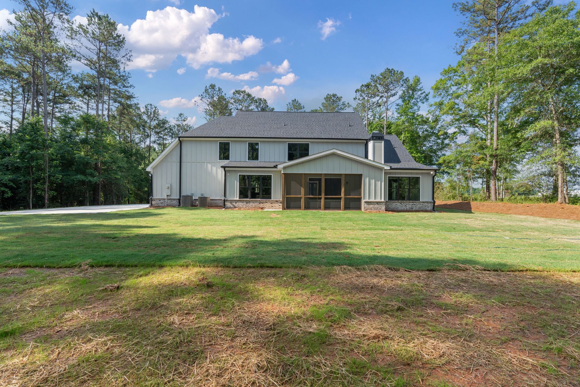 Two-story white house with green shutters and a screened porch on a grassy lot under a blue sky