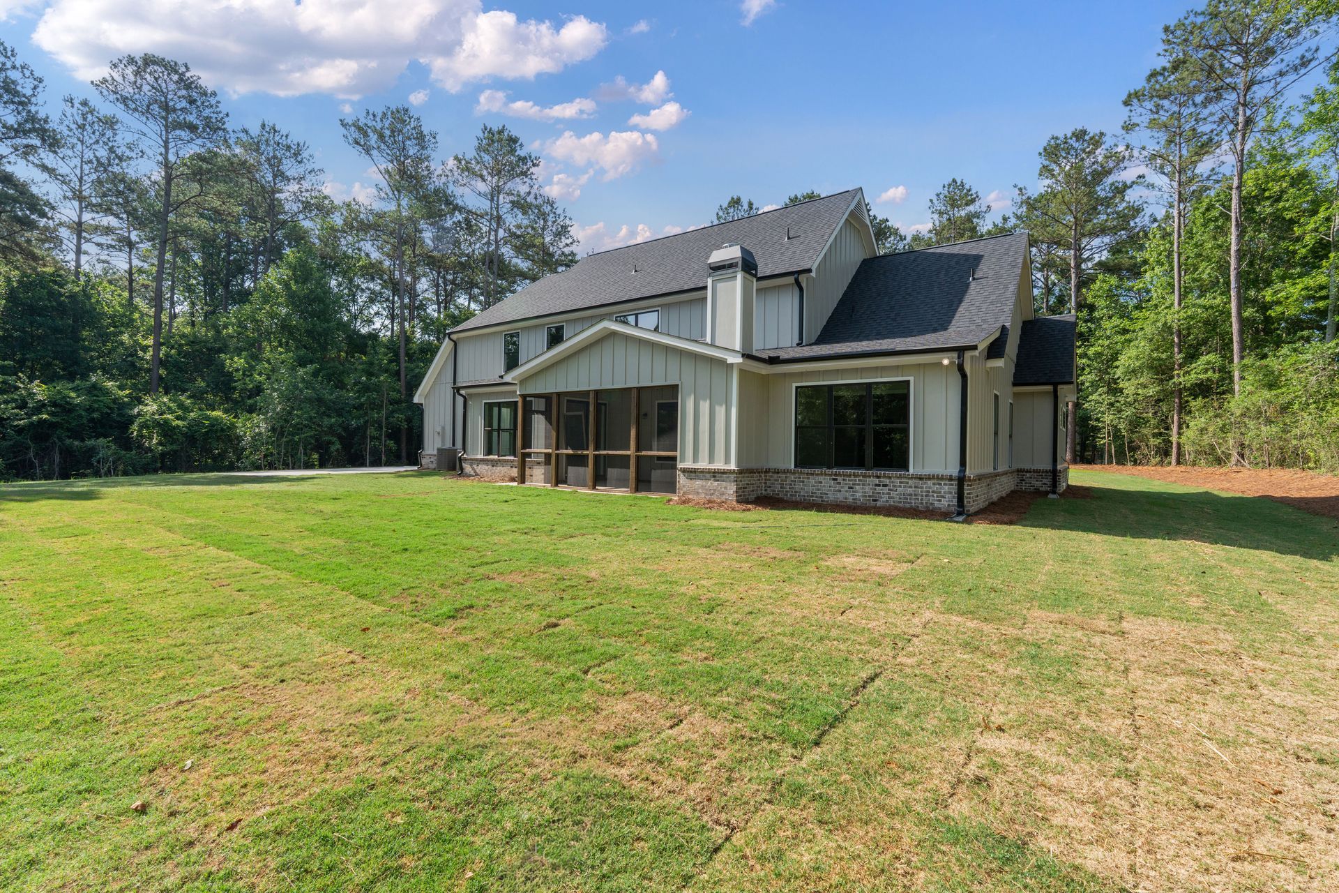 Modern house with gray siding and screened porch on a grassy lot surrounded by trees