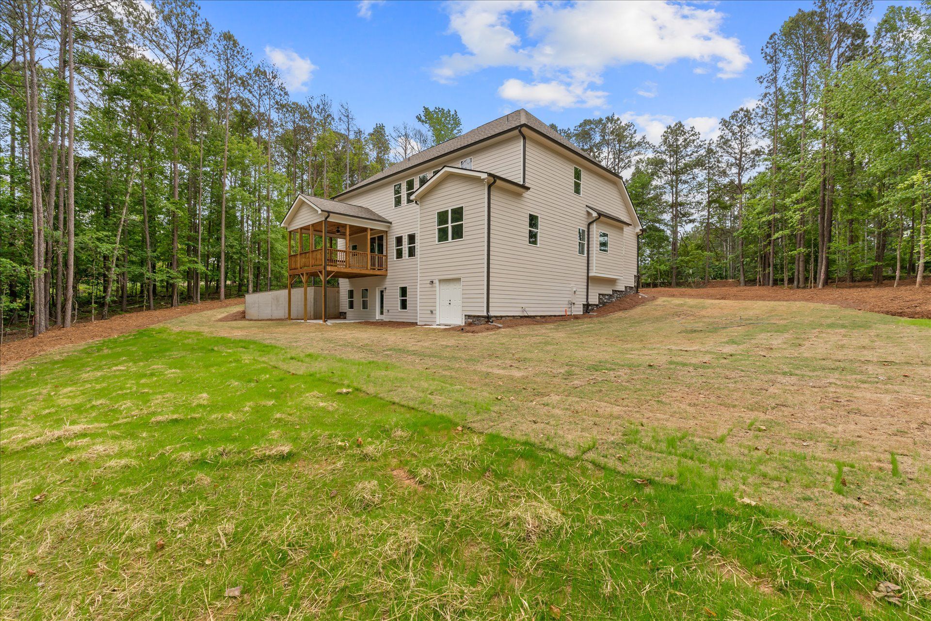 White house with porch and beige roof in a grassy yard, surrounded by trees under a partly cloudy sky