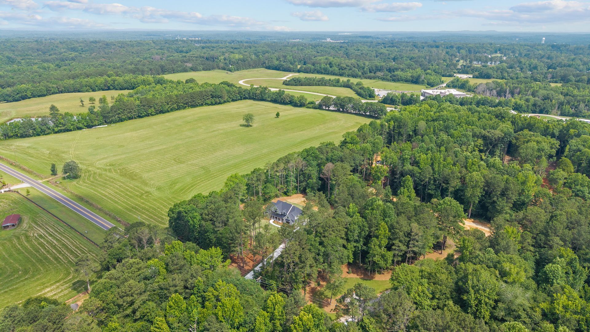 Aerial view of green farmland and forest with a small house in the center