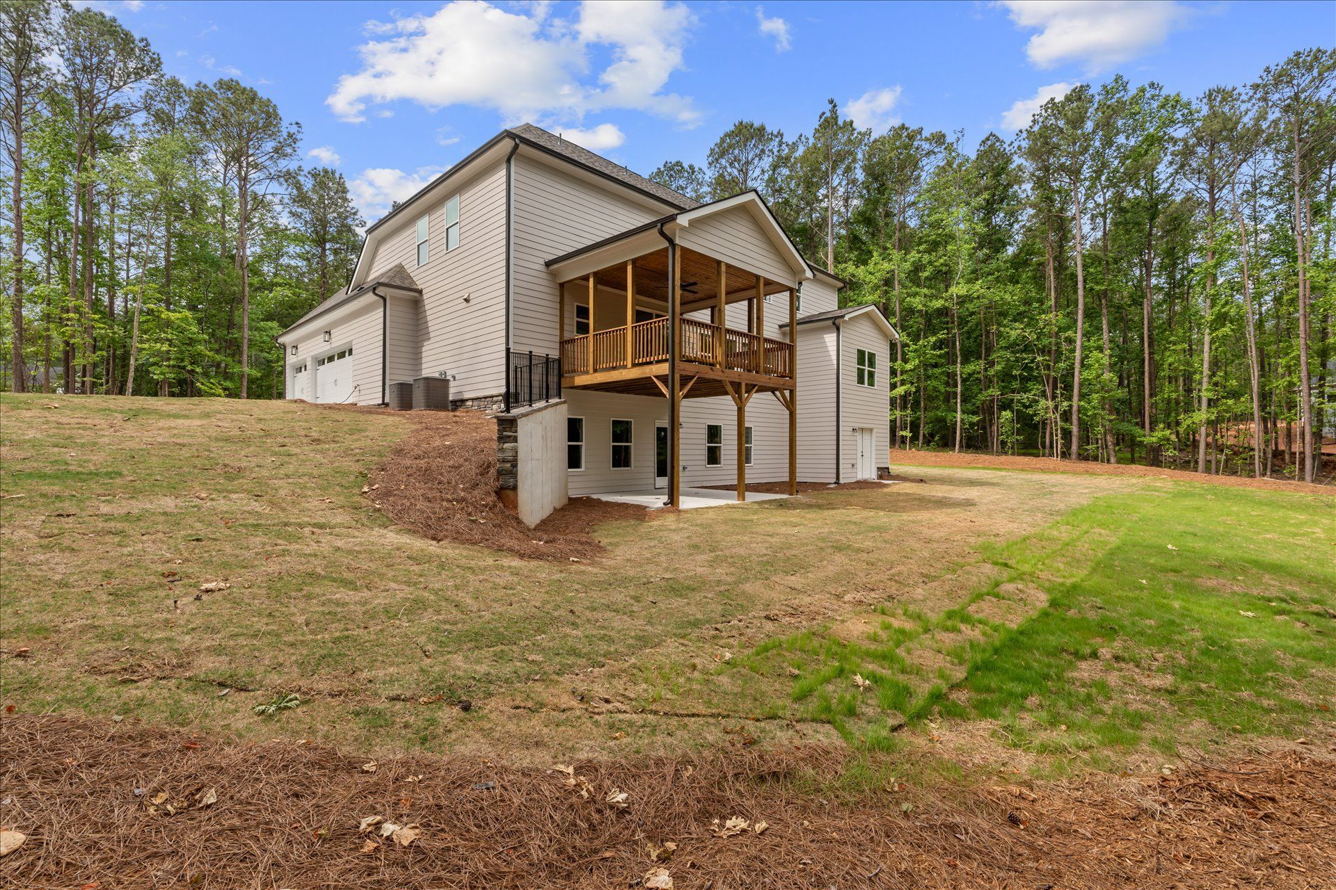 New white house with covered deck on a grassy hillside, surrounded by trees and blue sky