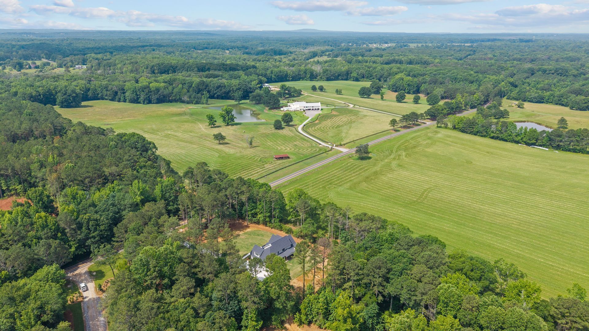 Aerial view of a green rural landscape with fields, trees, and a winding road under a cloudy sky