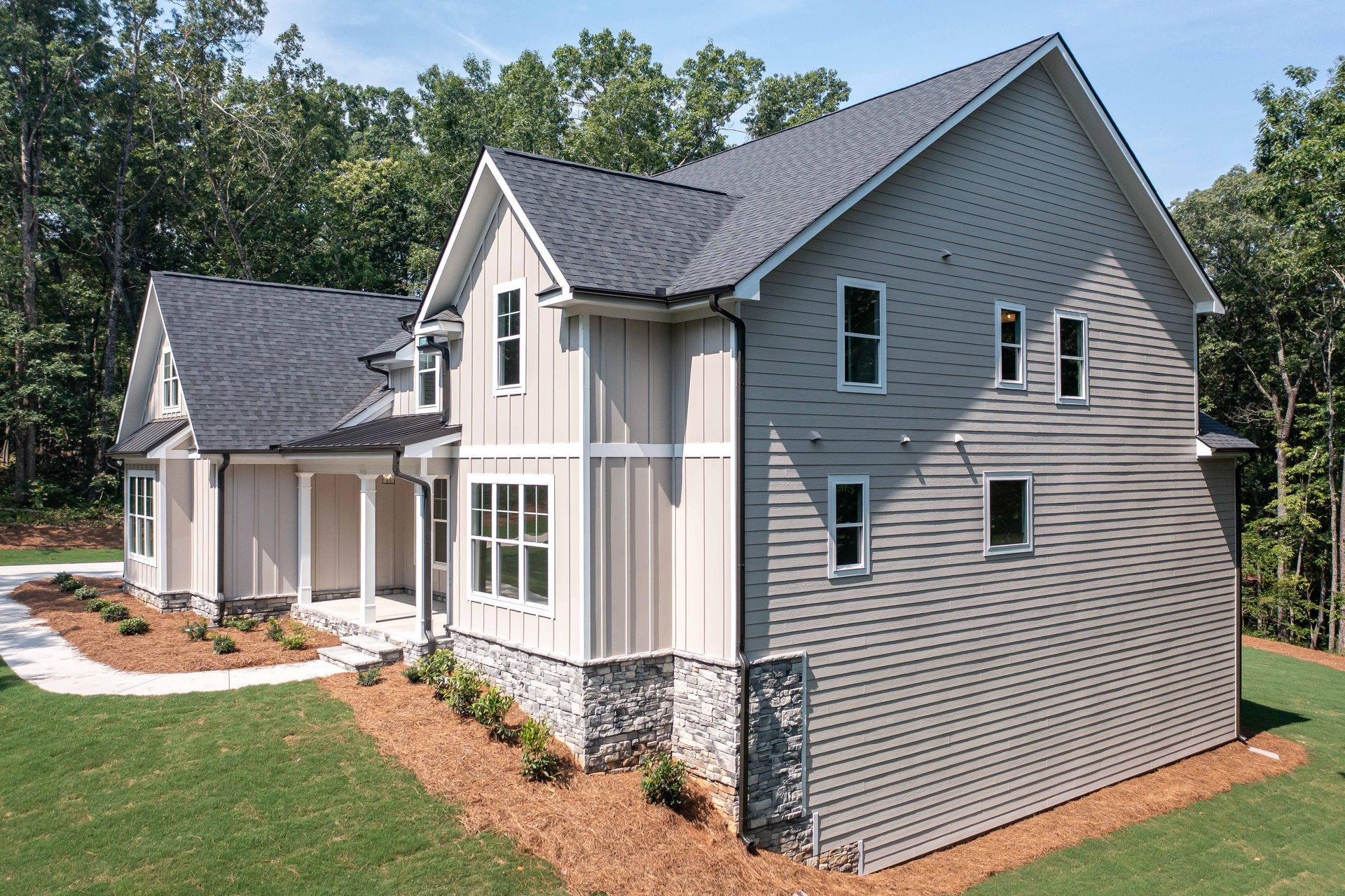 Gray two-story house with white trim and stone foundation, surrounded by lawn and trees