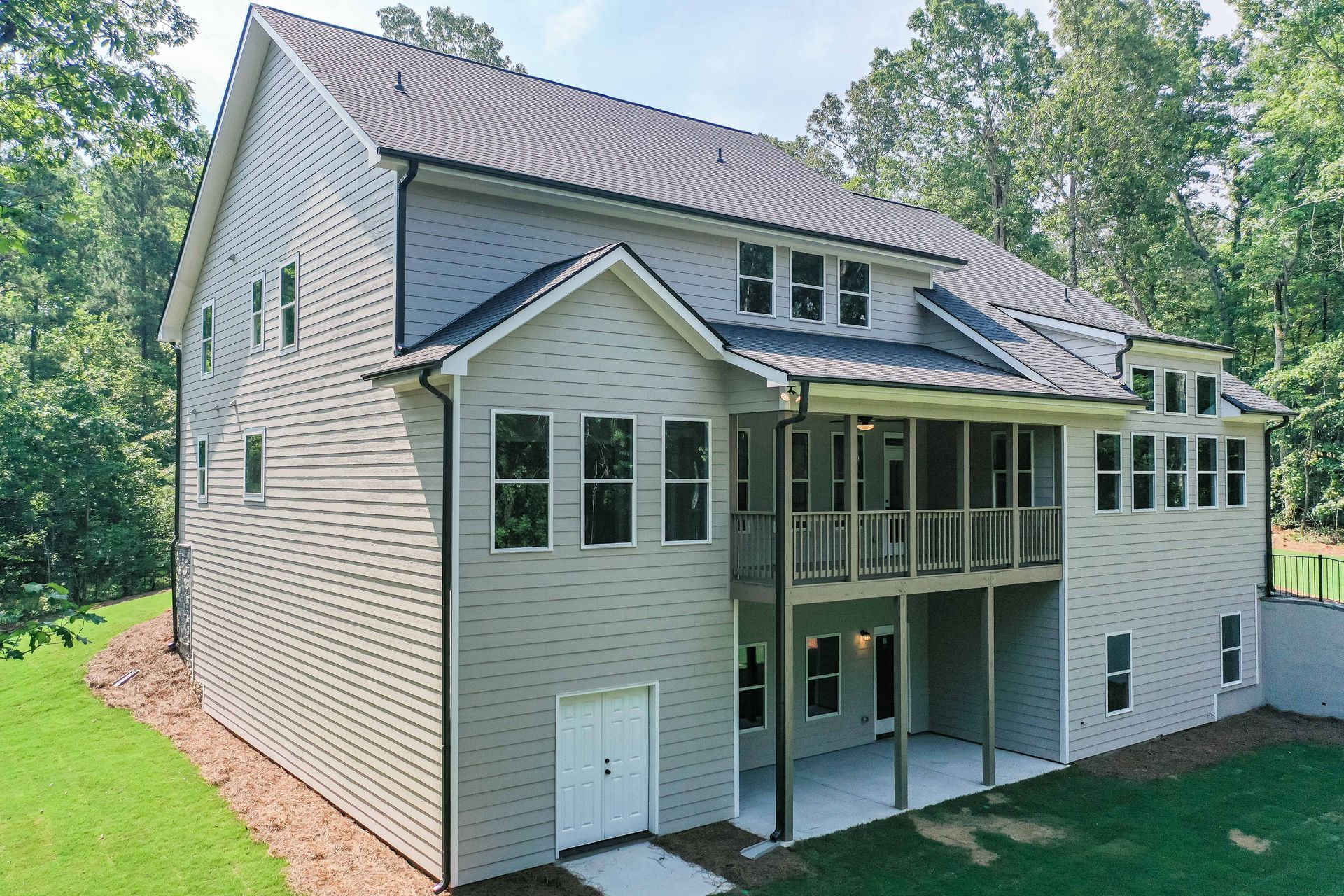 Exterior of a two-story beige house with screened porch and deck, surrounded by trees and lawn