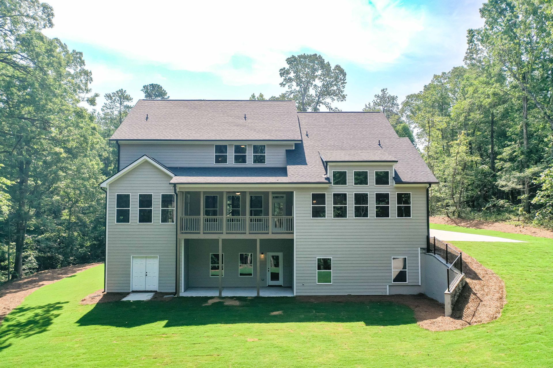 Rear view of a gray two-story house with a screened porch, surrounded by green lawn and trees