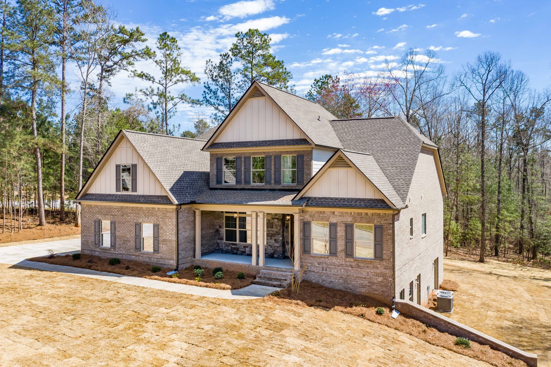 New two-story brick house under construction, surrounded by trees and dirt lot