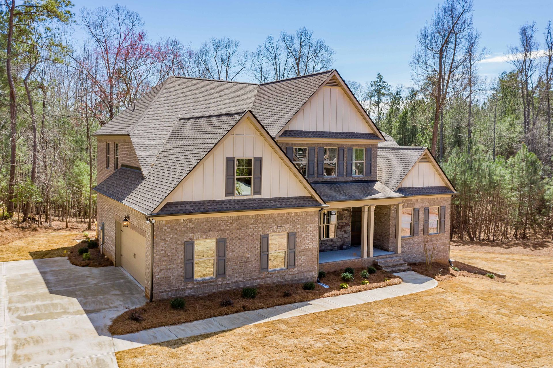 New stone-and-siding suburban house with gabled roof and front porch in a wooded lot