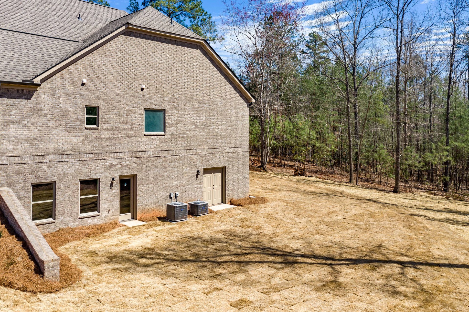 Stone house beside a cleared dirt yard with trees and blue sky
