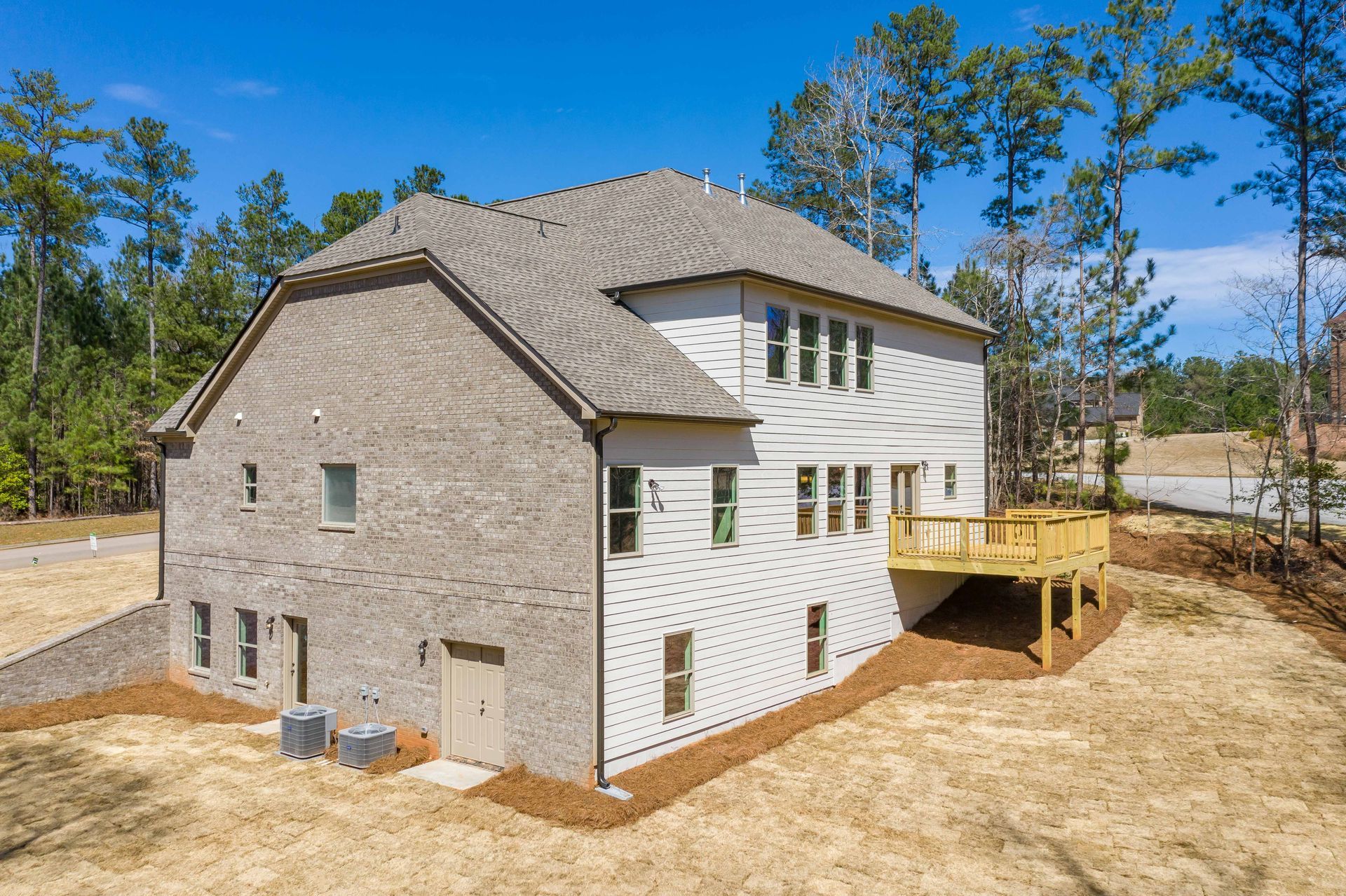 New two-story house with stone and white siding, wooden deck, and dirt yard under a blue sky