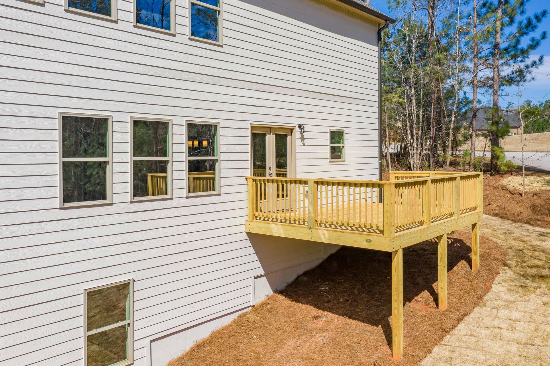 White house exterior with a raised wooden deck and stairs over a mulched yard.