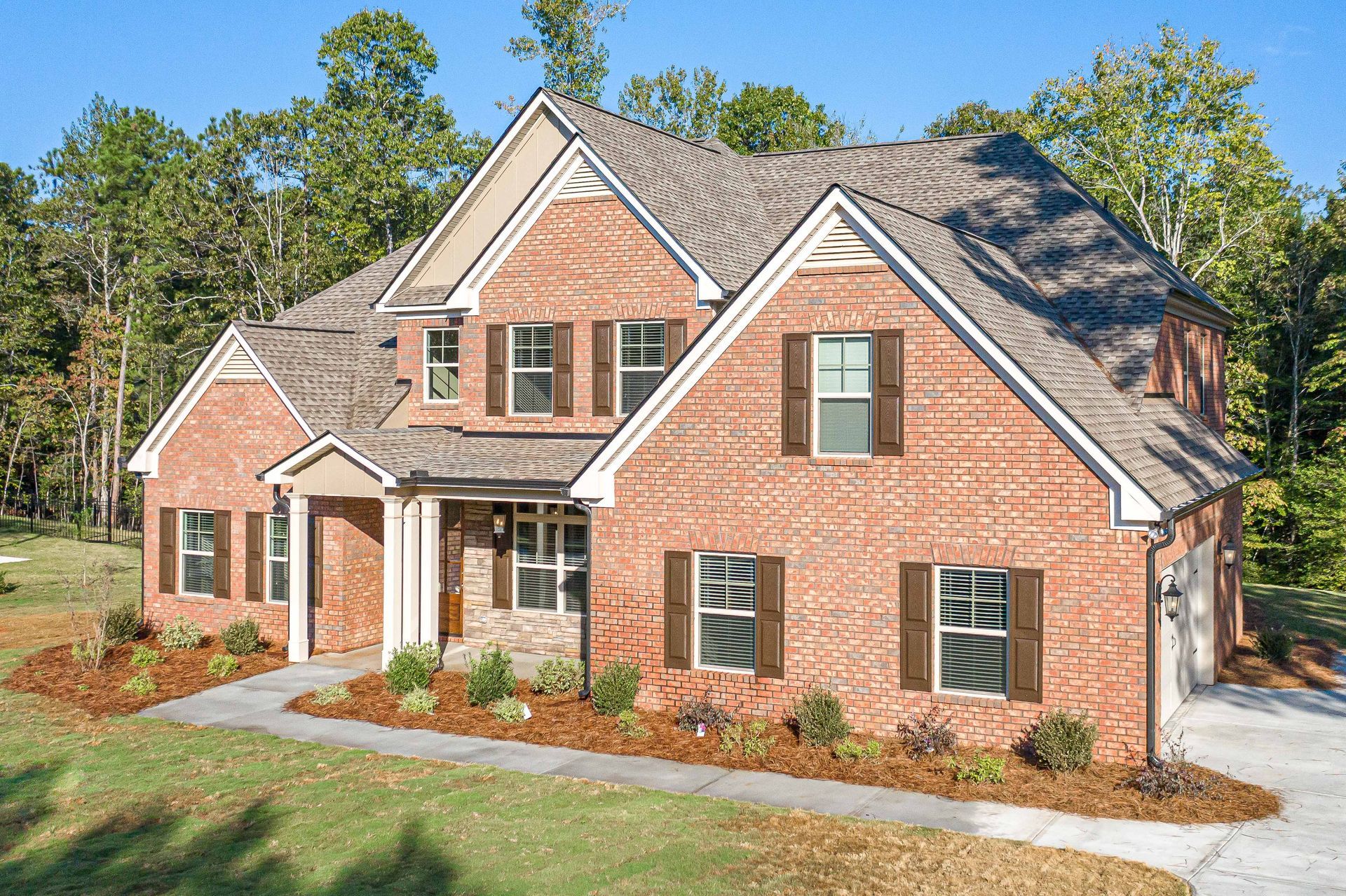 Brick two-story suburban house with gabled roof and front porch, surrounded by trees and lawn
