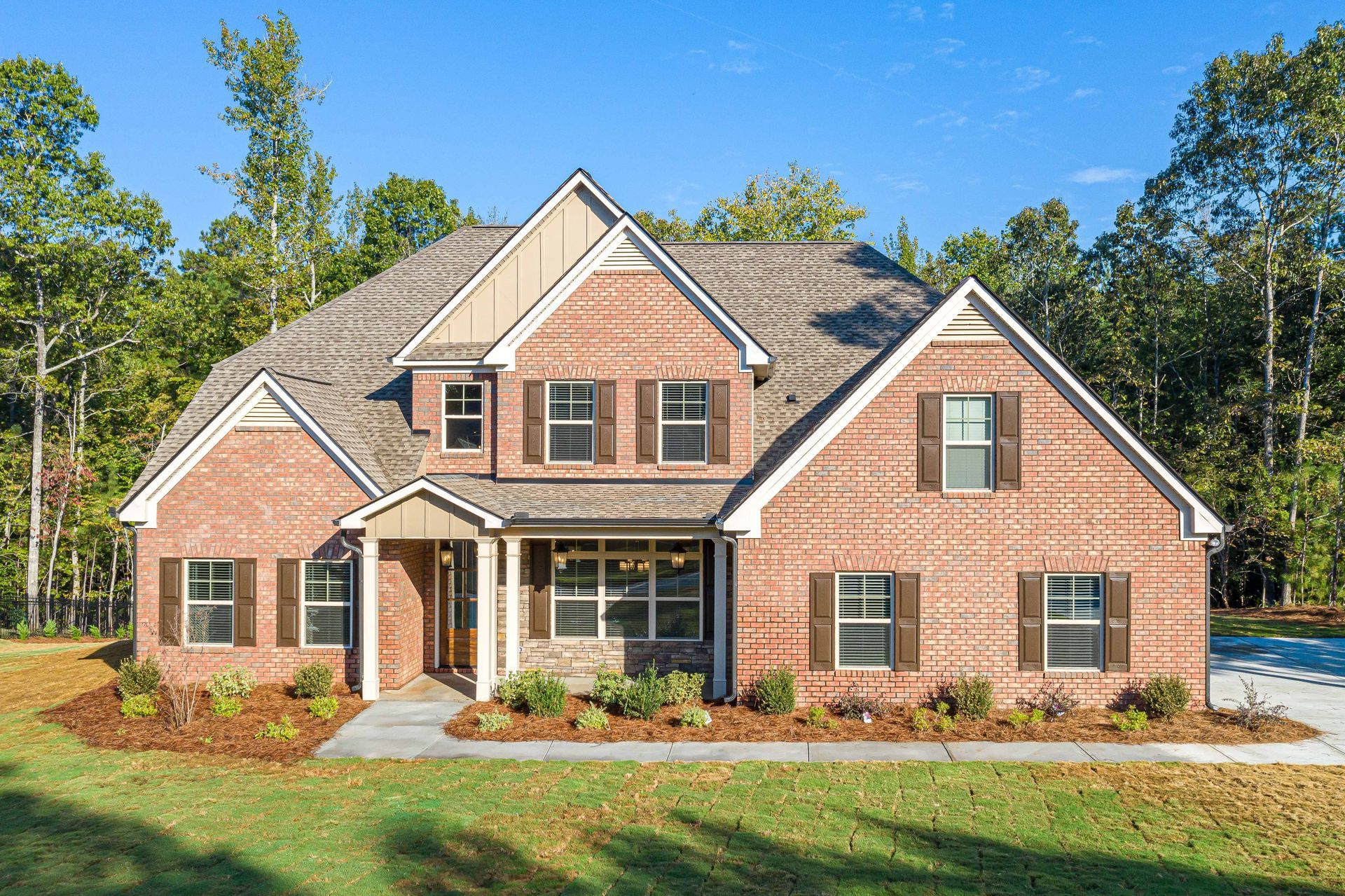 Brick suburban house with gabled roof, front porch, and landscaped yard under a clear blue sky