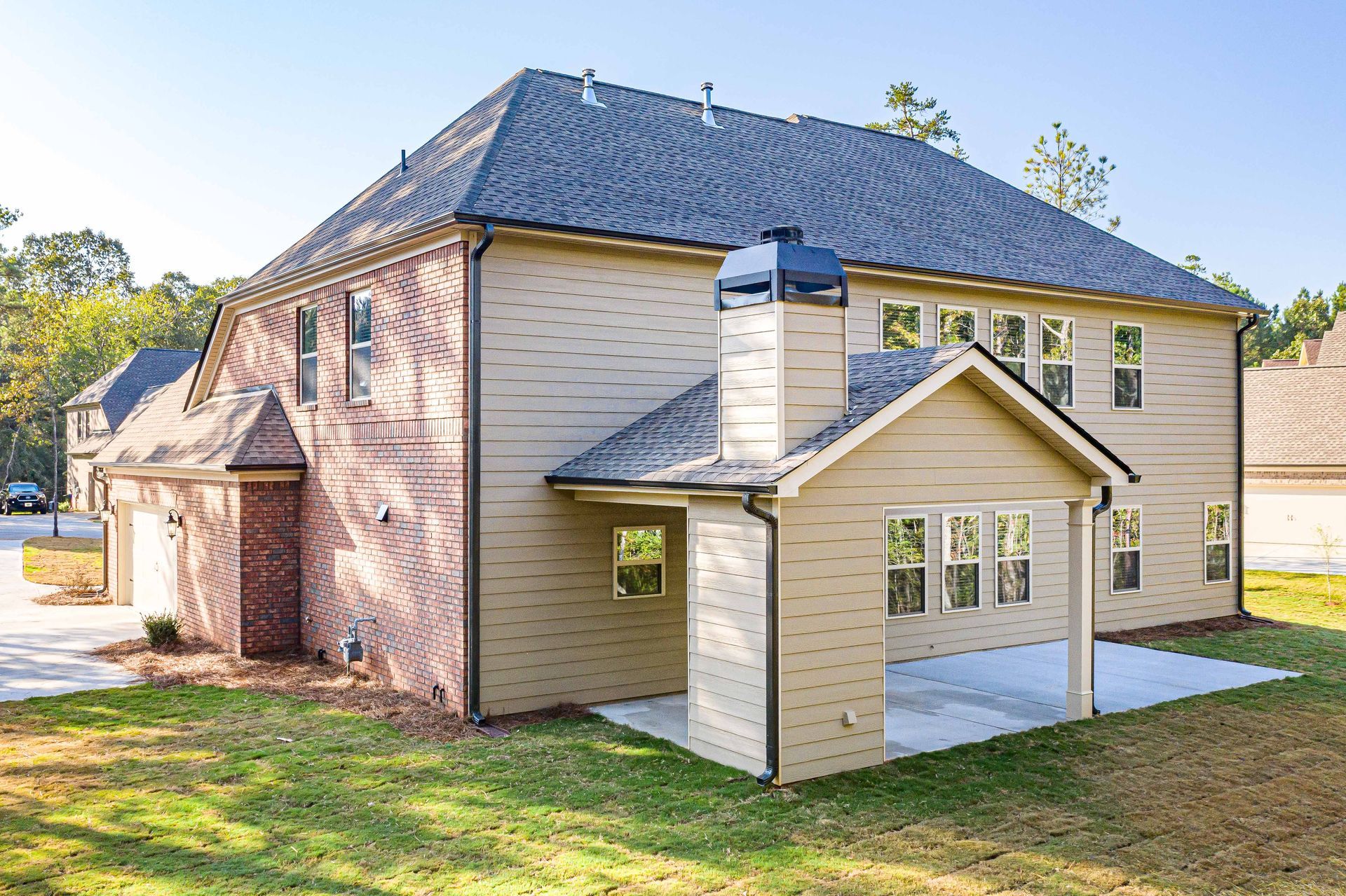 Brick two-story house with beige siding, dark roof, and covered front entry on a grassy lot