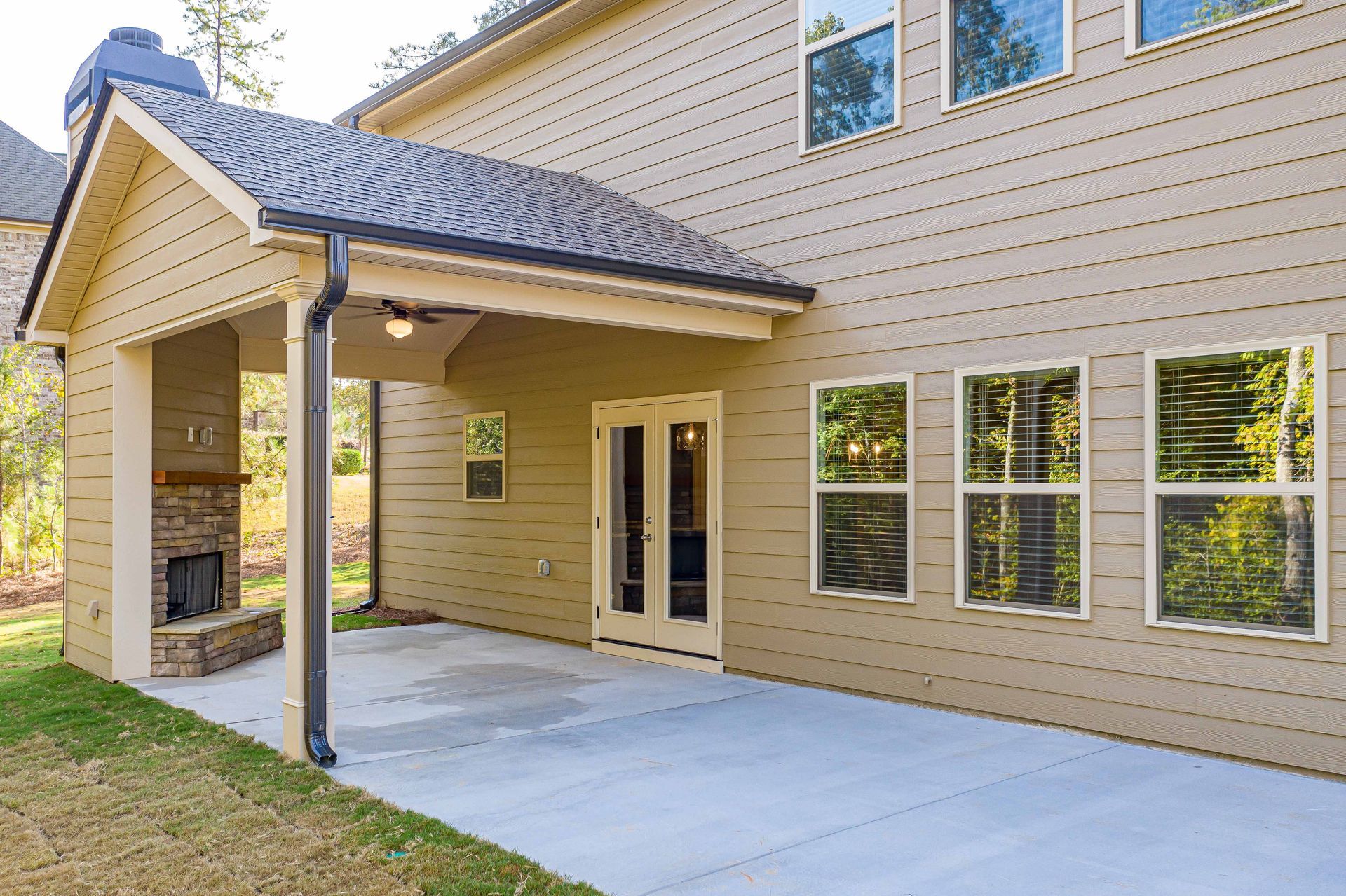Covered patio beside tan two-story house with concrete slab and multiple windows