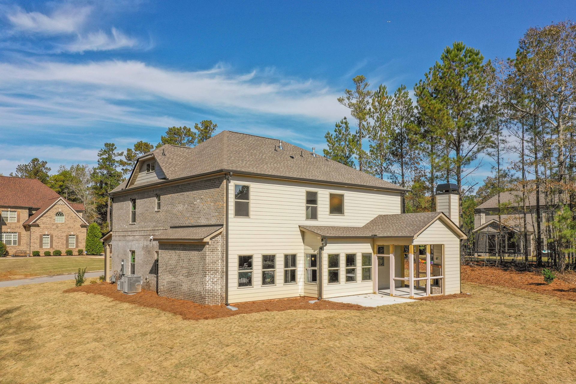 Suburban two-story house with white siding, stone accents, and a small covered porch in a wooded yard