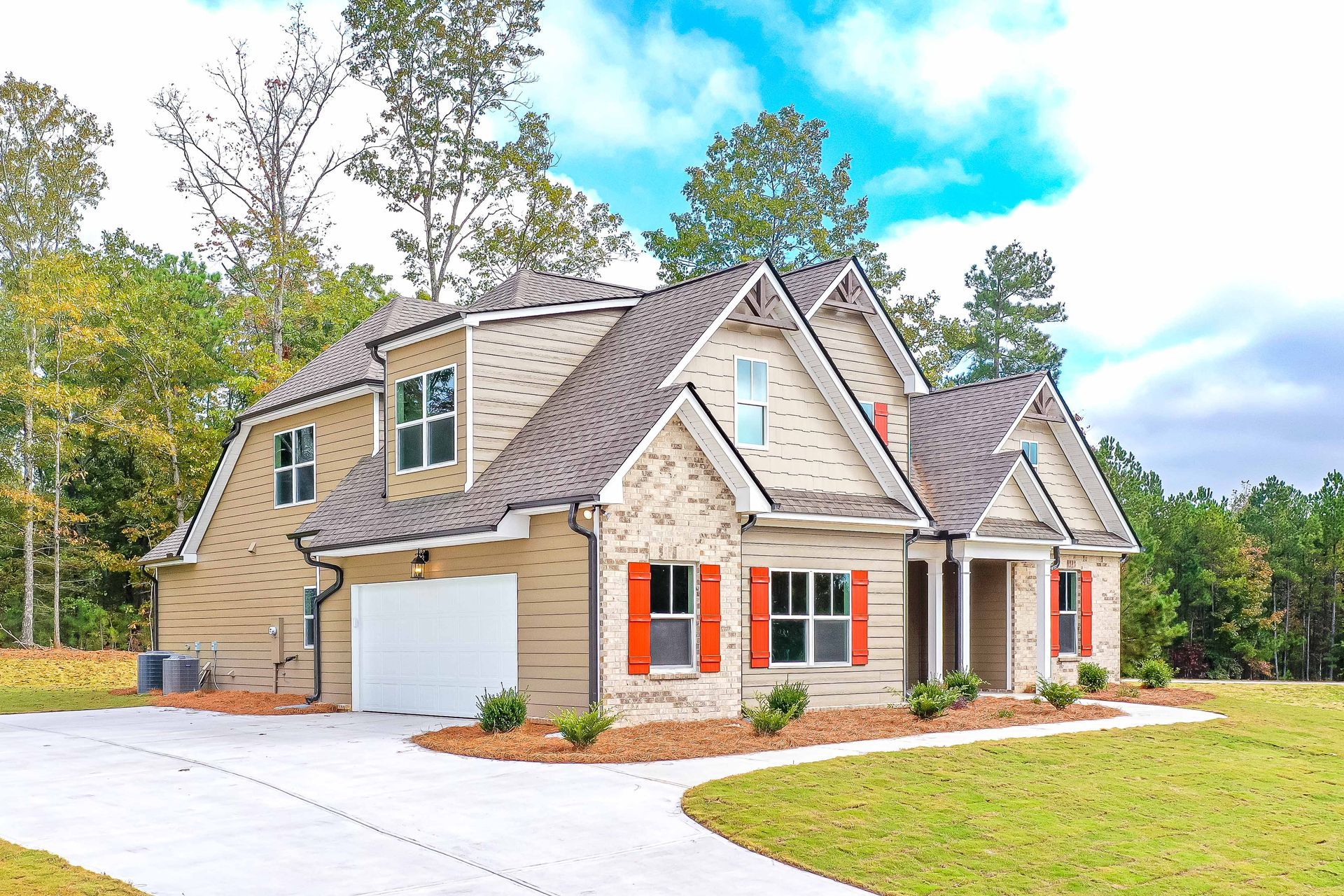 Modern beige house with stone accents, white garage, orange shutters, and a landscaped yard under a blue sky