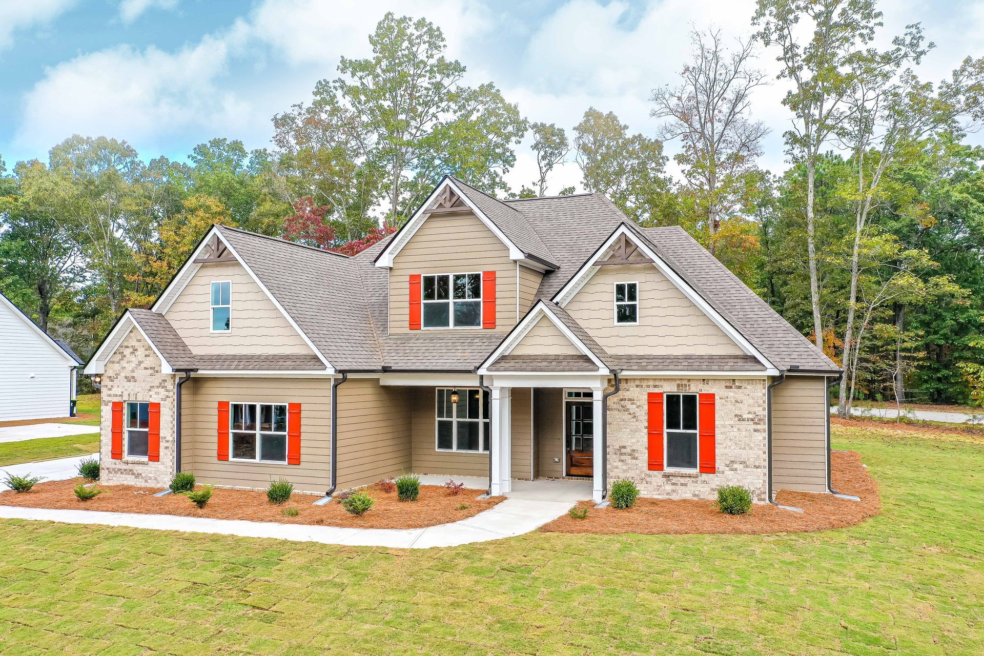 Suburban brick house with gray roof, orange shutters, and a front porch, surrounded by lawn and trees