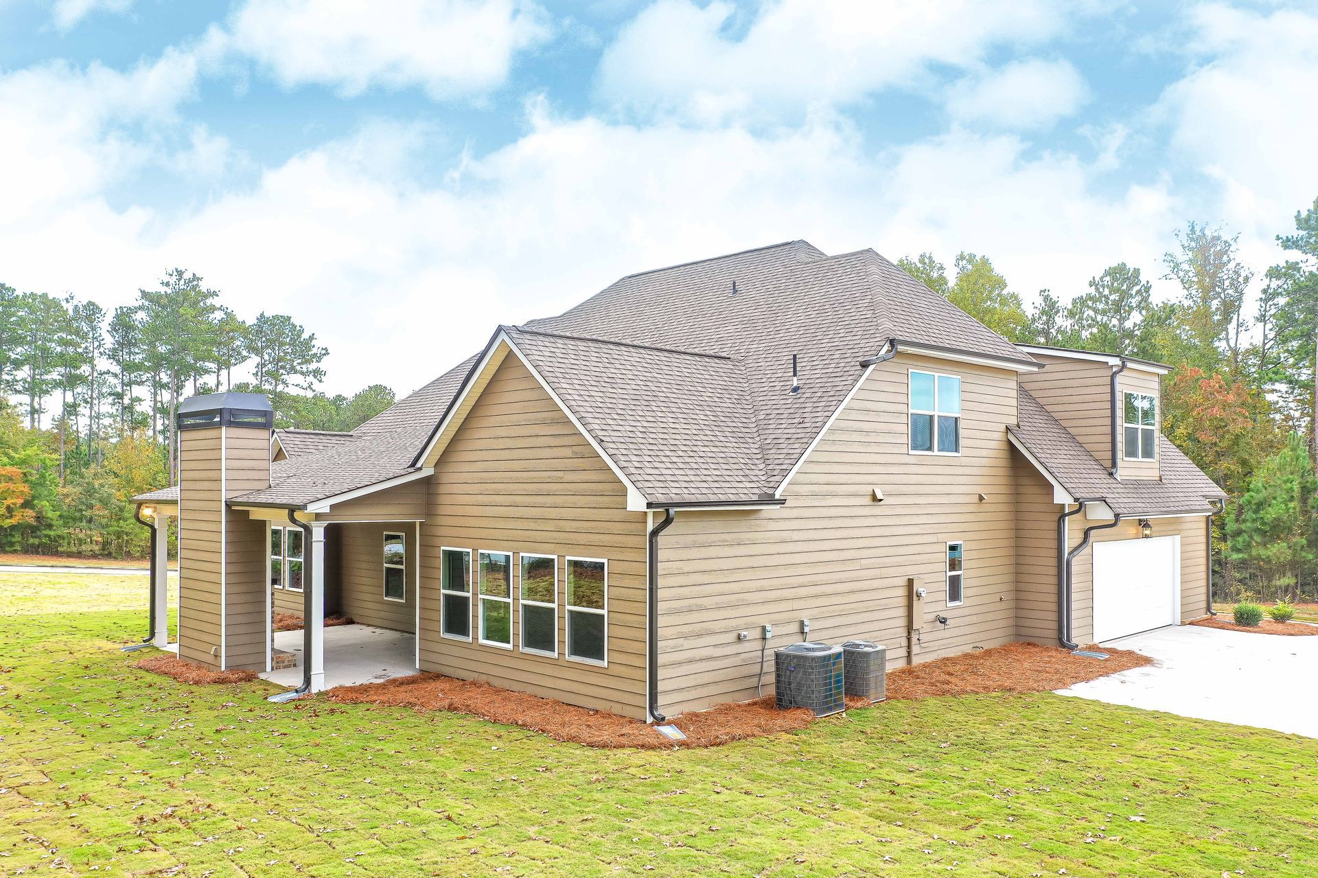Modern beige brick house with dark roof, garage, and covered patio on a grassy lot