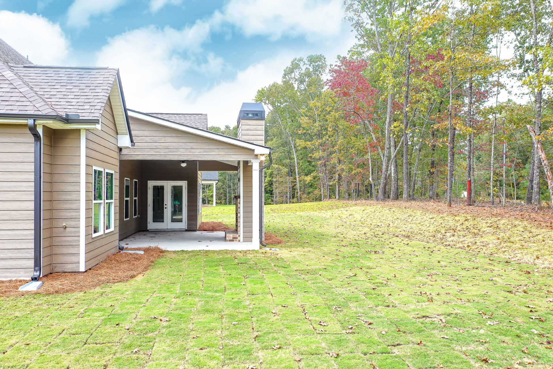 Backyard view of a house with a covered patio and grassy lawn beside trees in autumn colors