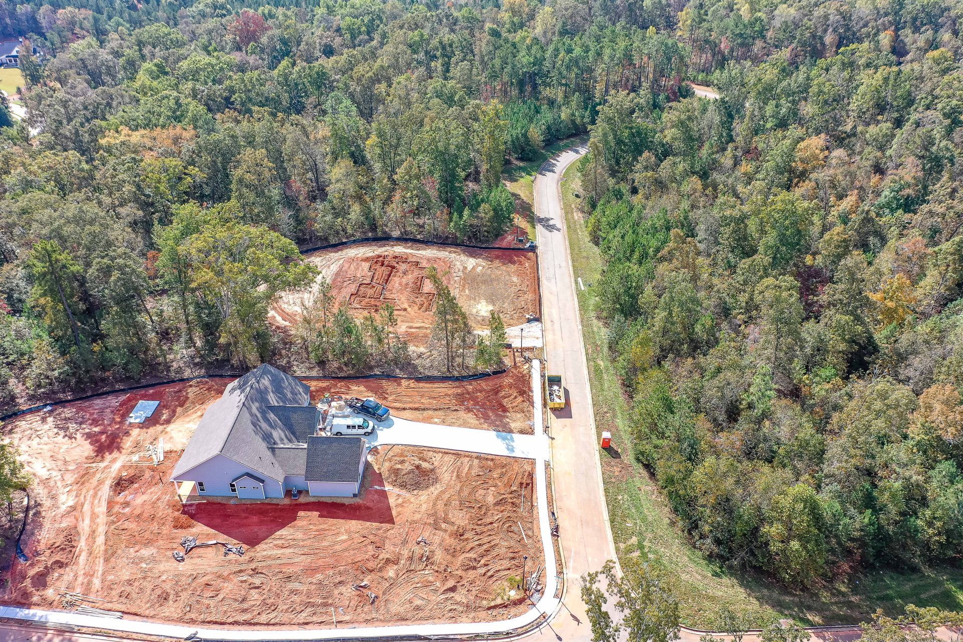 Aerial view of a house under construction beside a rural road, surrounded by dense trees.