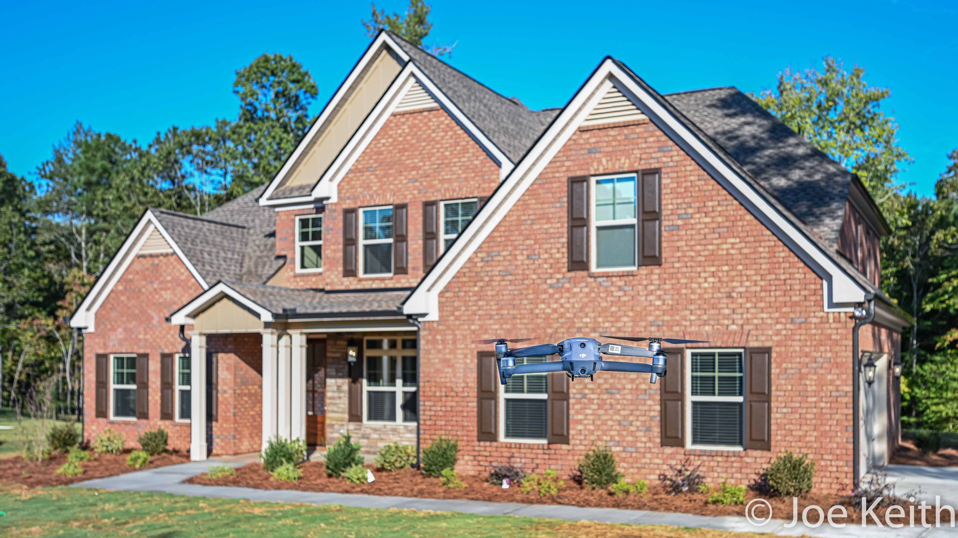 Brick suburban house with gabled roof, white trim, and landscaped front yard under a blue sky