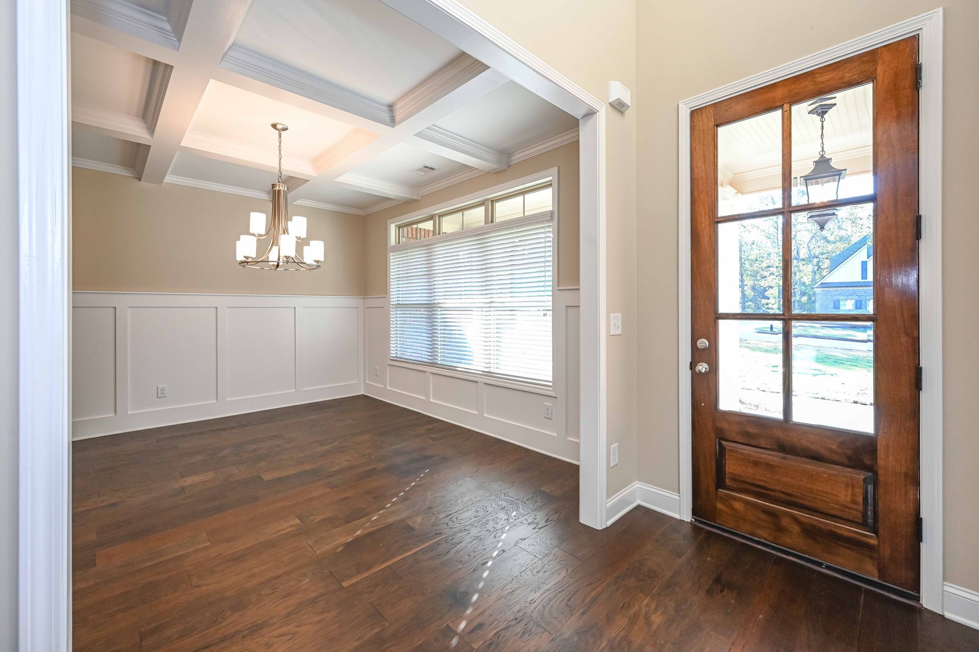 Empty dining room with hardwood floors, tray ceiling, chandelier, and wood-framed glass door to a snowy view
