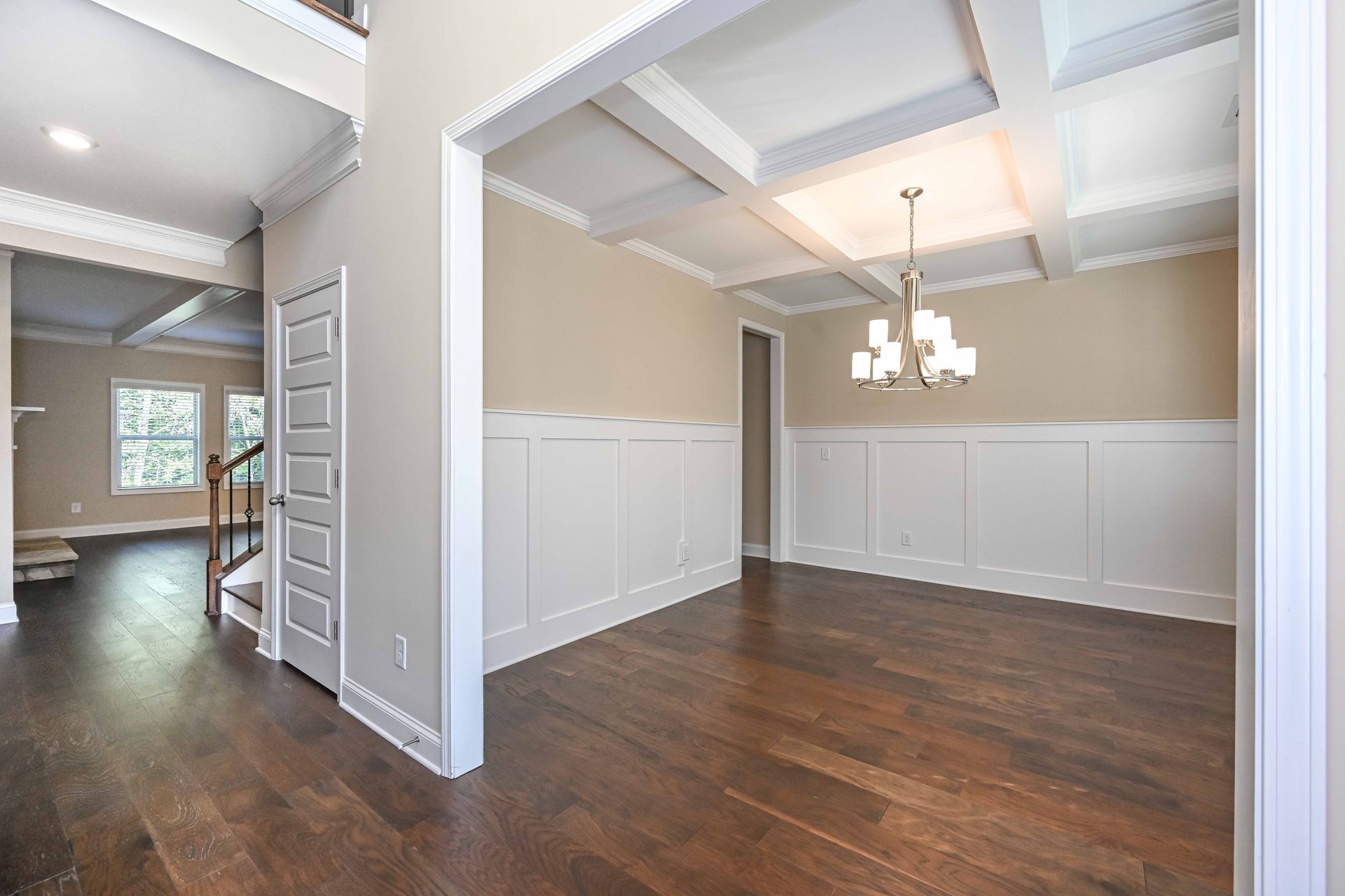 Empty dining room with dark hardwood floors, white wainscoting, coffered ceiling, and chandelier
