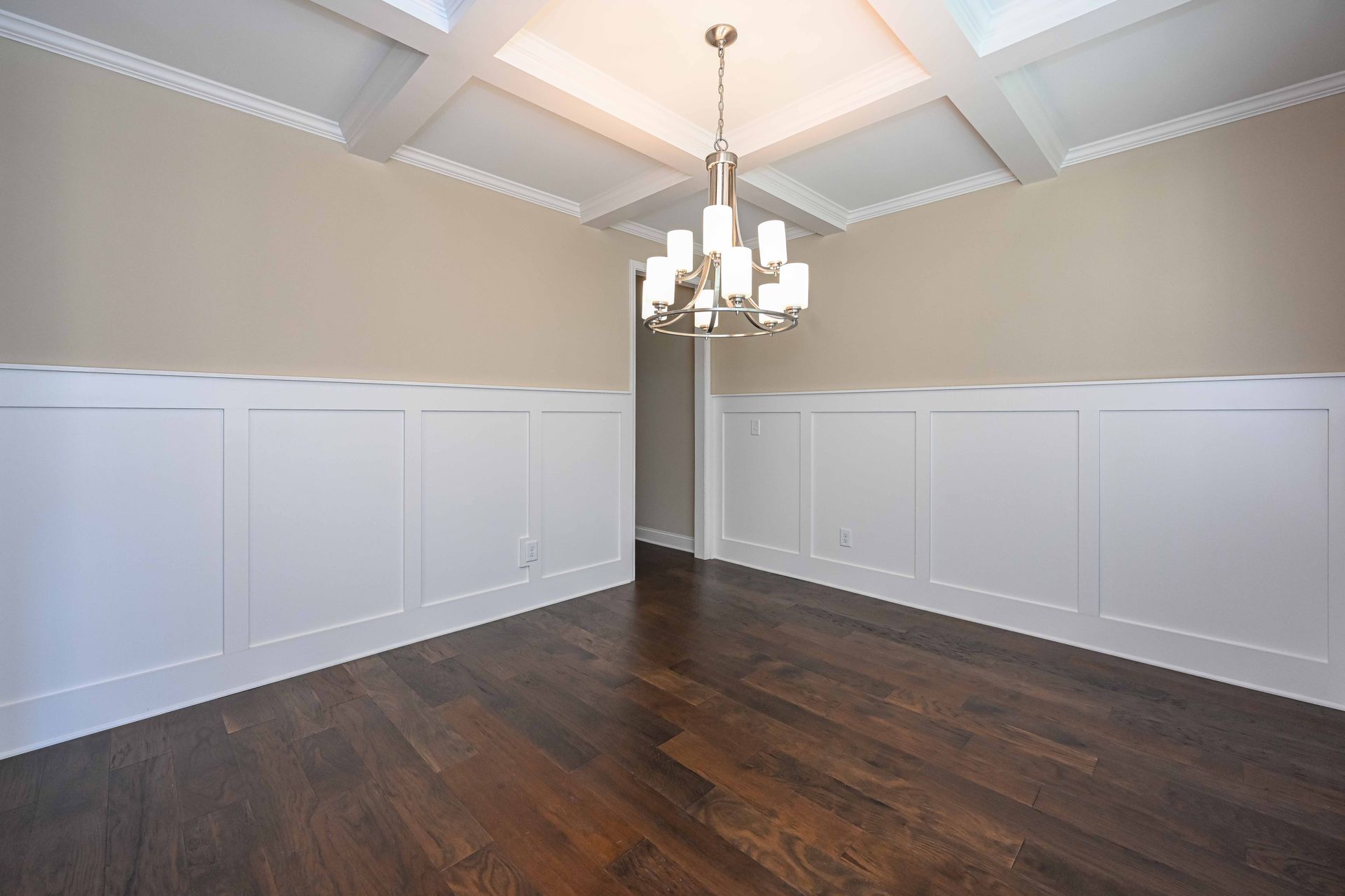 Empty dining room with dark hardwood floors, white wainscoting, beige walls, and a chandelier under a tray ceiling