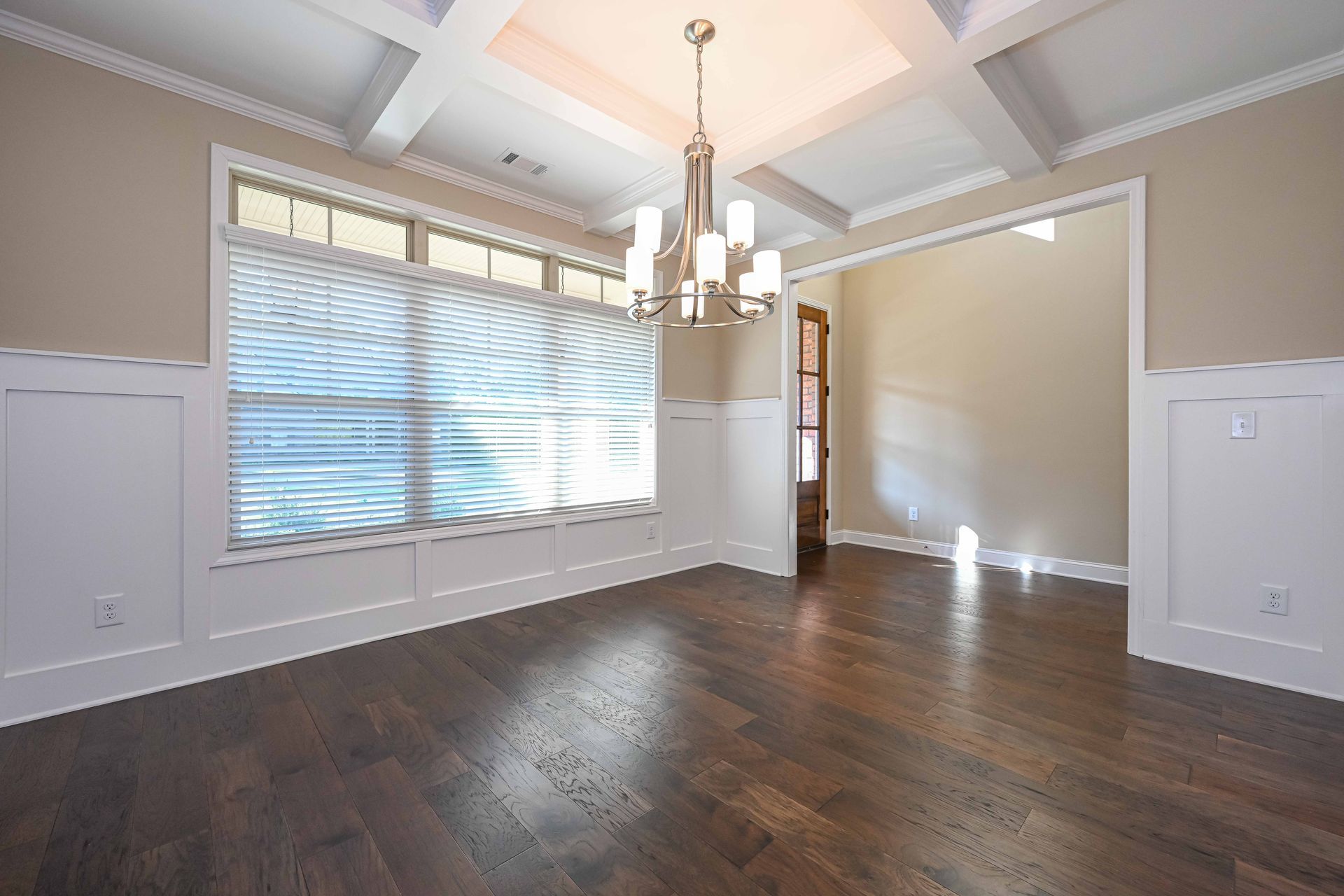 Empty dining room with dark wood floors, large window blinds, and a chandelier against beige walls