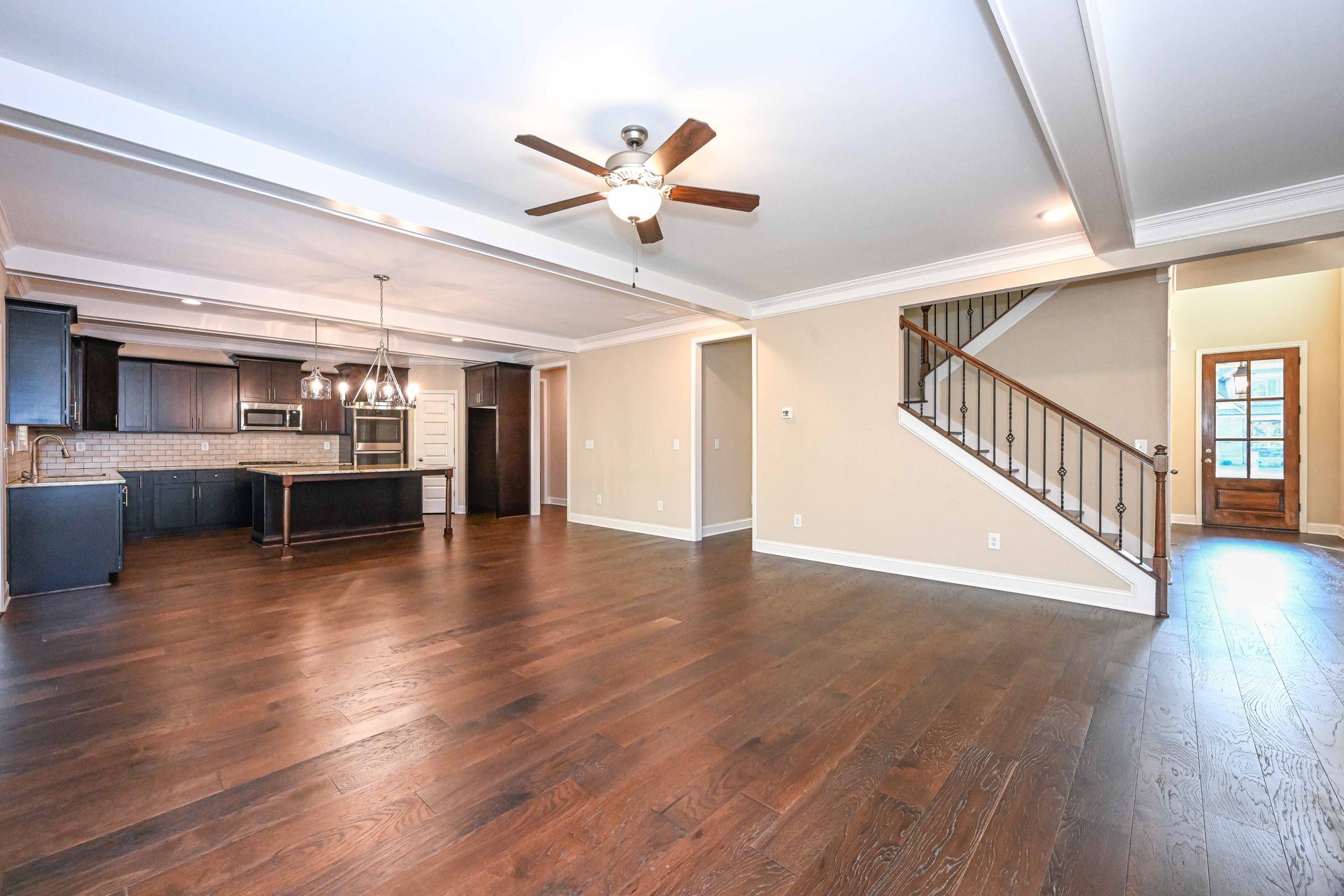 Open-plan living room with dark wood floors, kitchen, staircase, and ceiling fan