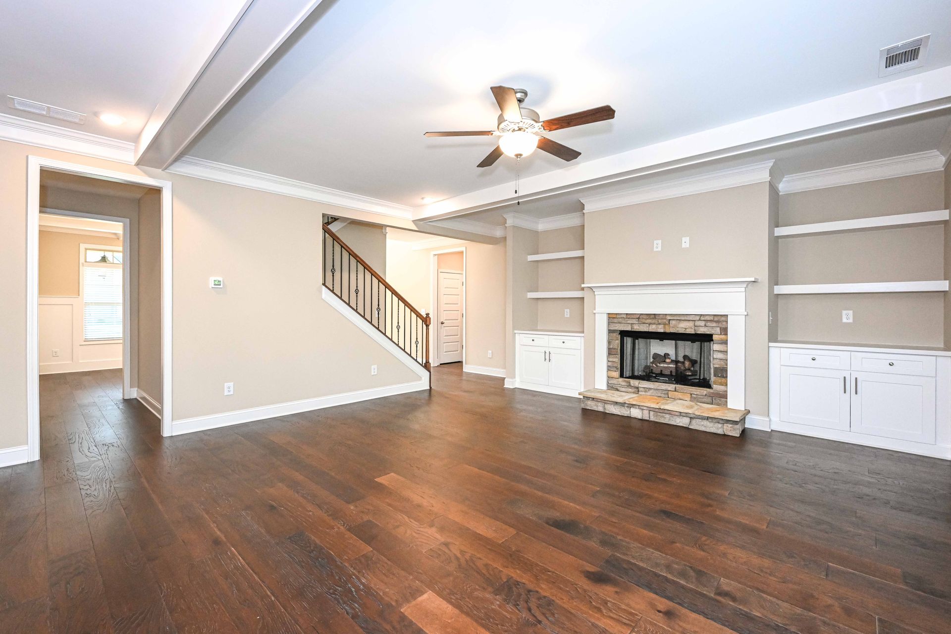 Spacious living room with hardwood floors, beige walls, ceiling fan, fireplace, and built-in shelves