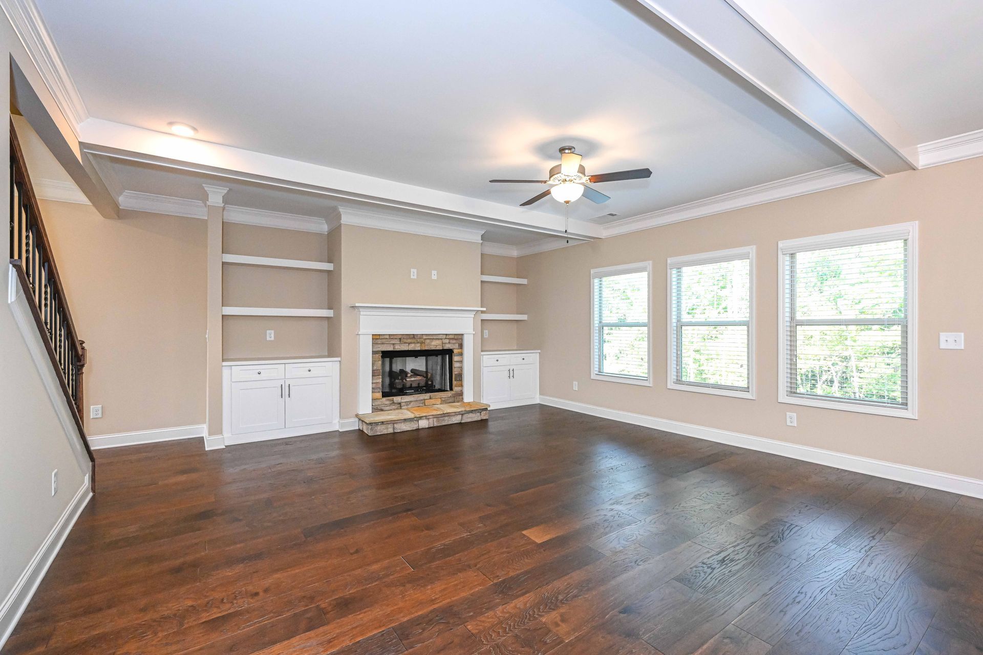 Spacious living room with dark wood floors, fireplace, built-in shelves, and large windows.
