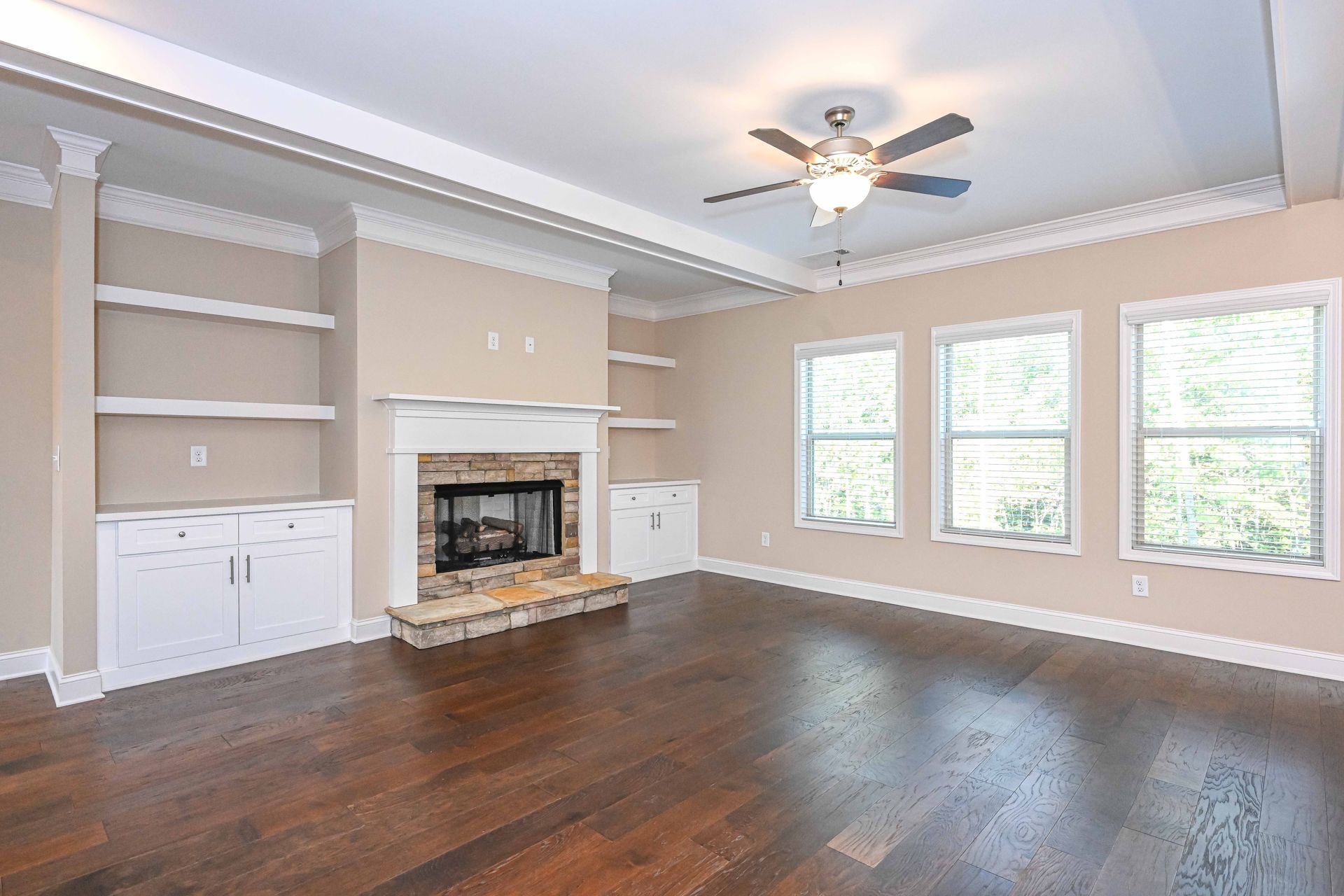 Spacious living room with dark wood floors, white built-ins, a fireplace, and large windows.