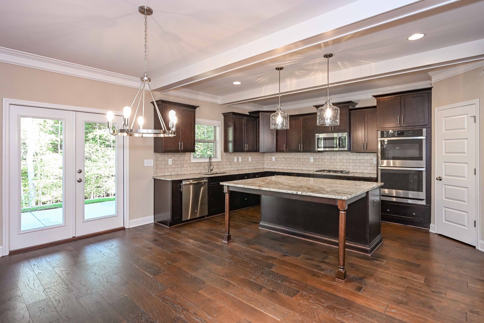 Spacious modern kitchen with dark cabinets, large island, hardwood floors, and French doors to the outside