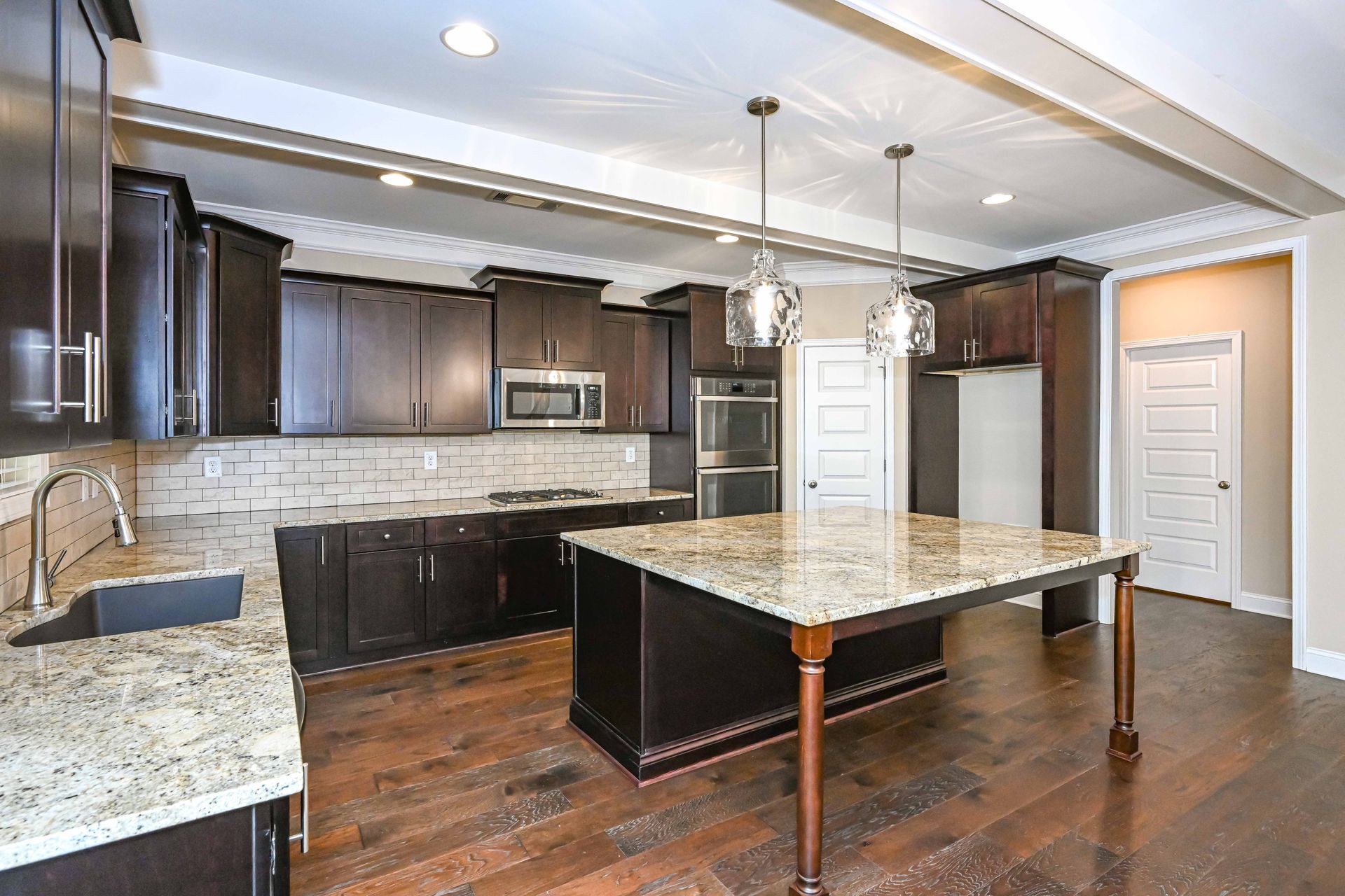 Modern kitchen with dark wood cabinets, granite island, stainless appliances, and hardwood floors